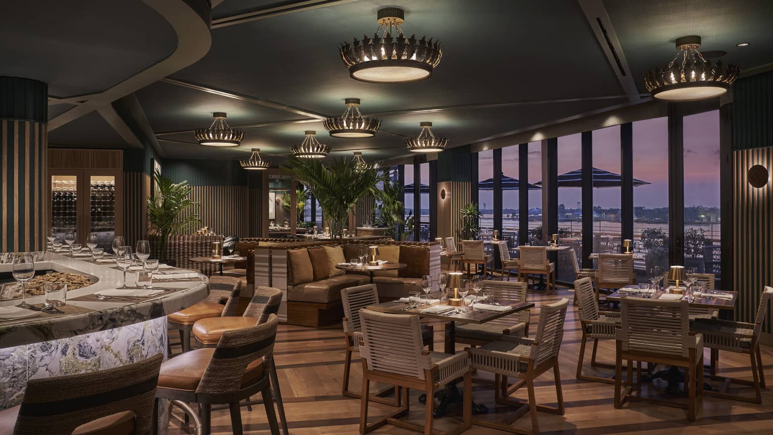 A dimly lit restaurant with a large bar, many tables and large windows.