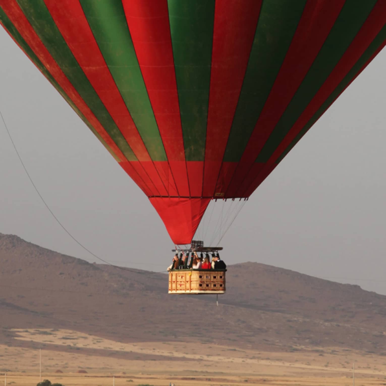 Man stands in field under large green and red hot air balloon