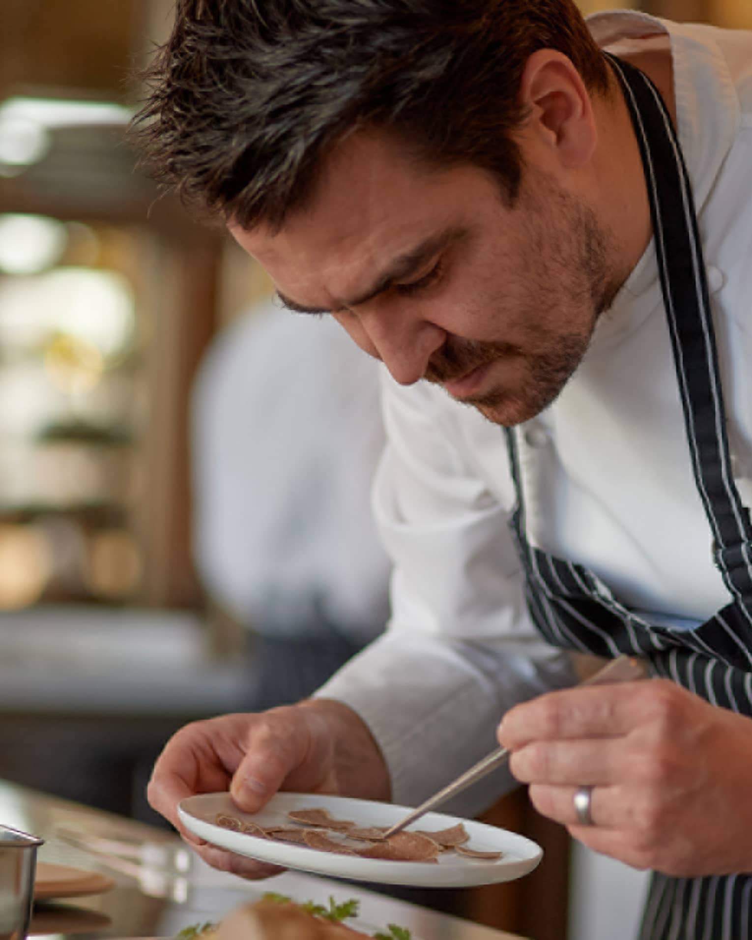 Four Seasons chef in striped apron carefully plating a dish in a kitchen