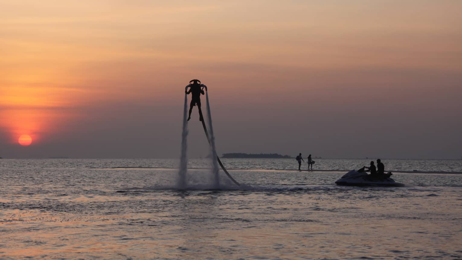 Silhouette of someone with X Jetpack suspended in air over water at sunset