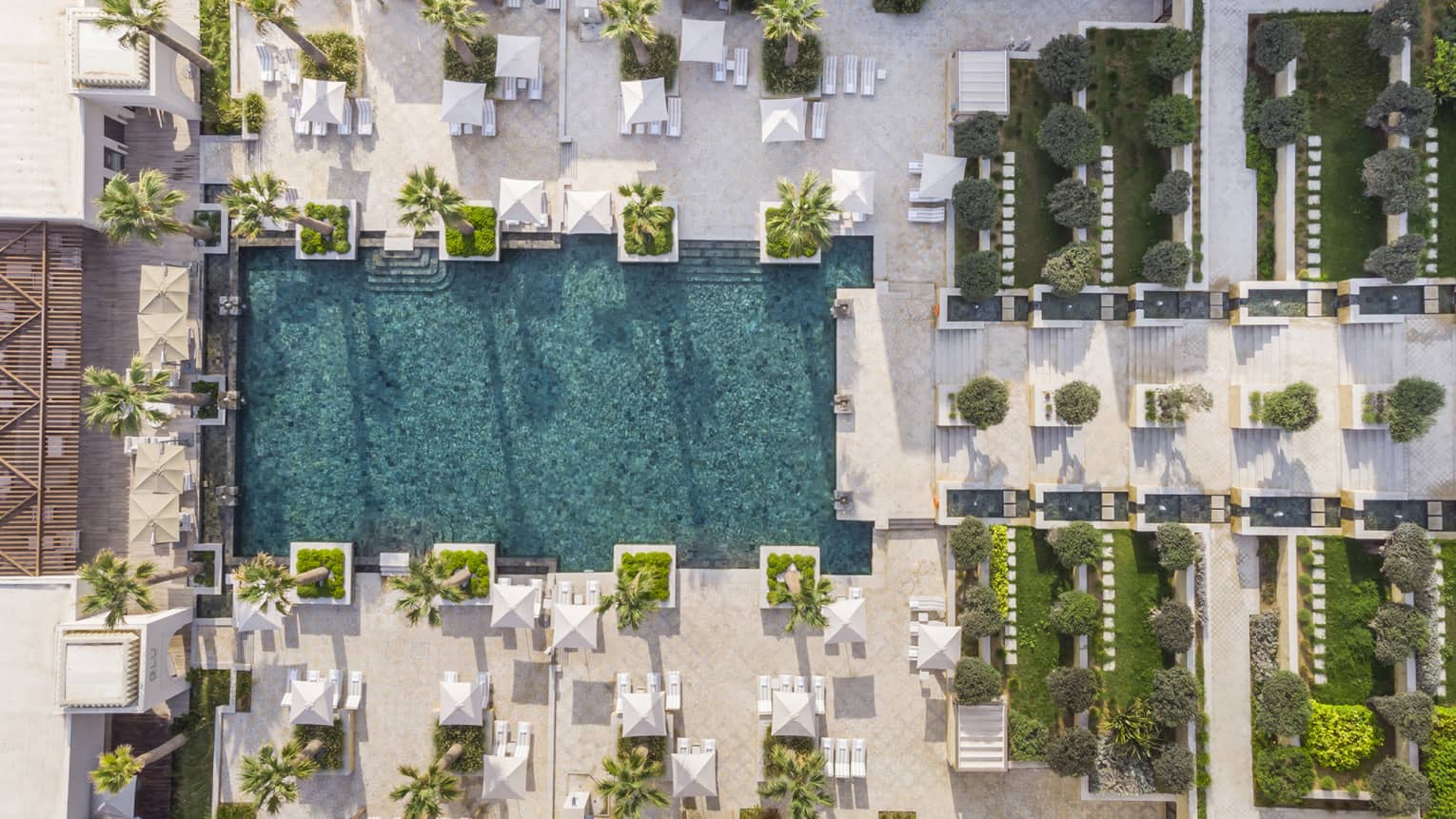 Aerial view of tiered walkway descending toward rectangular pool surrounded by palm trees