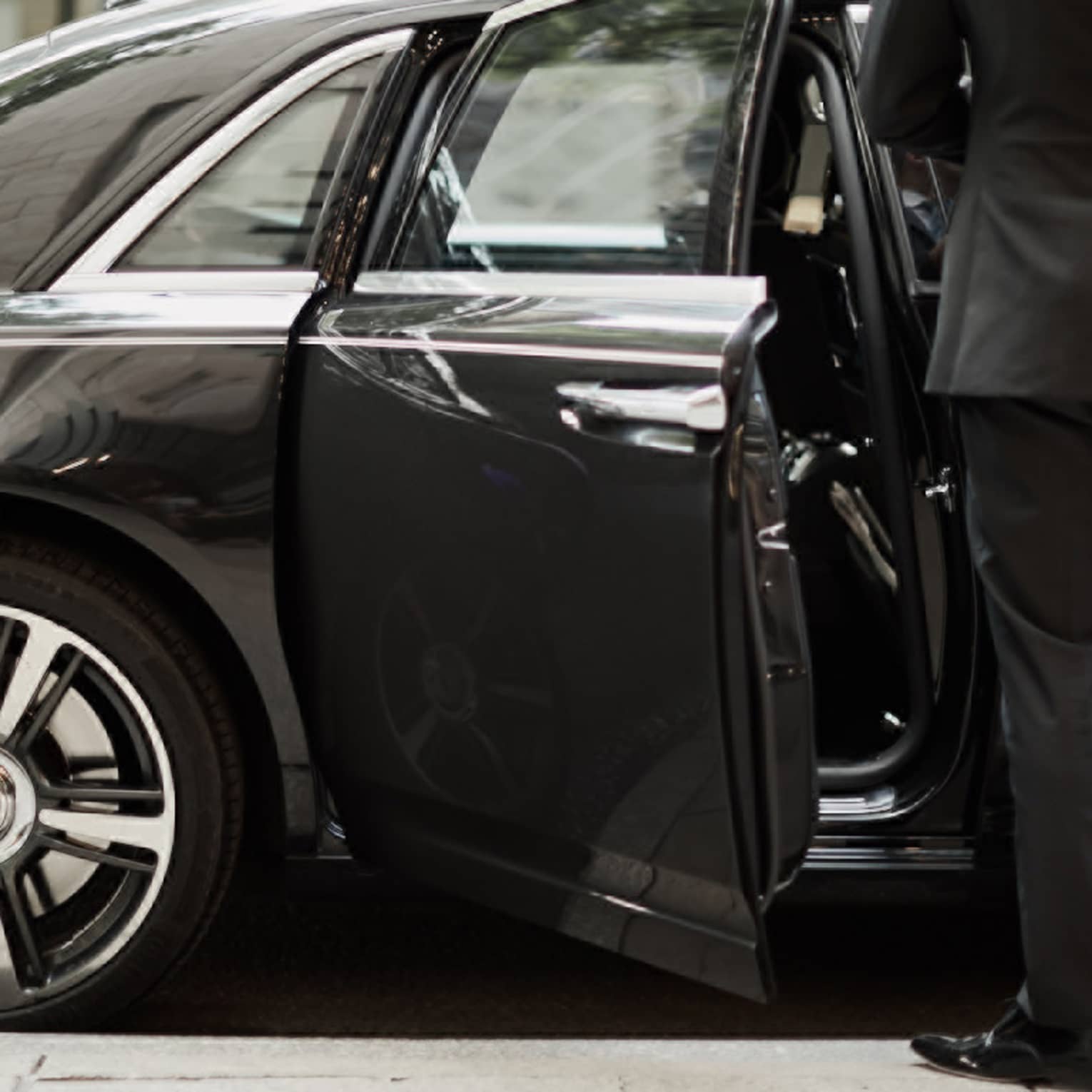 Man in suit by open door of black luxury car