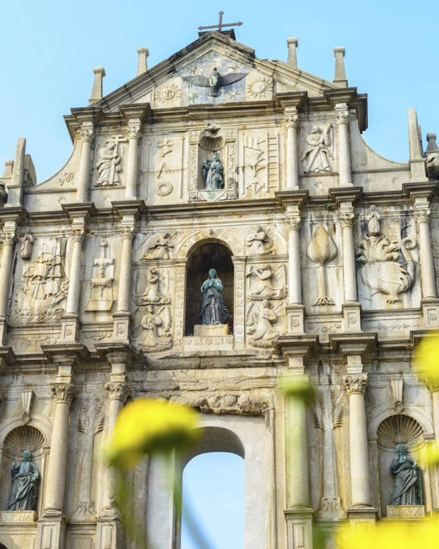 An ornate facade with archways at bottom, lined with thin towers and columns, intricate carvings and shelves holding statues.