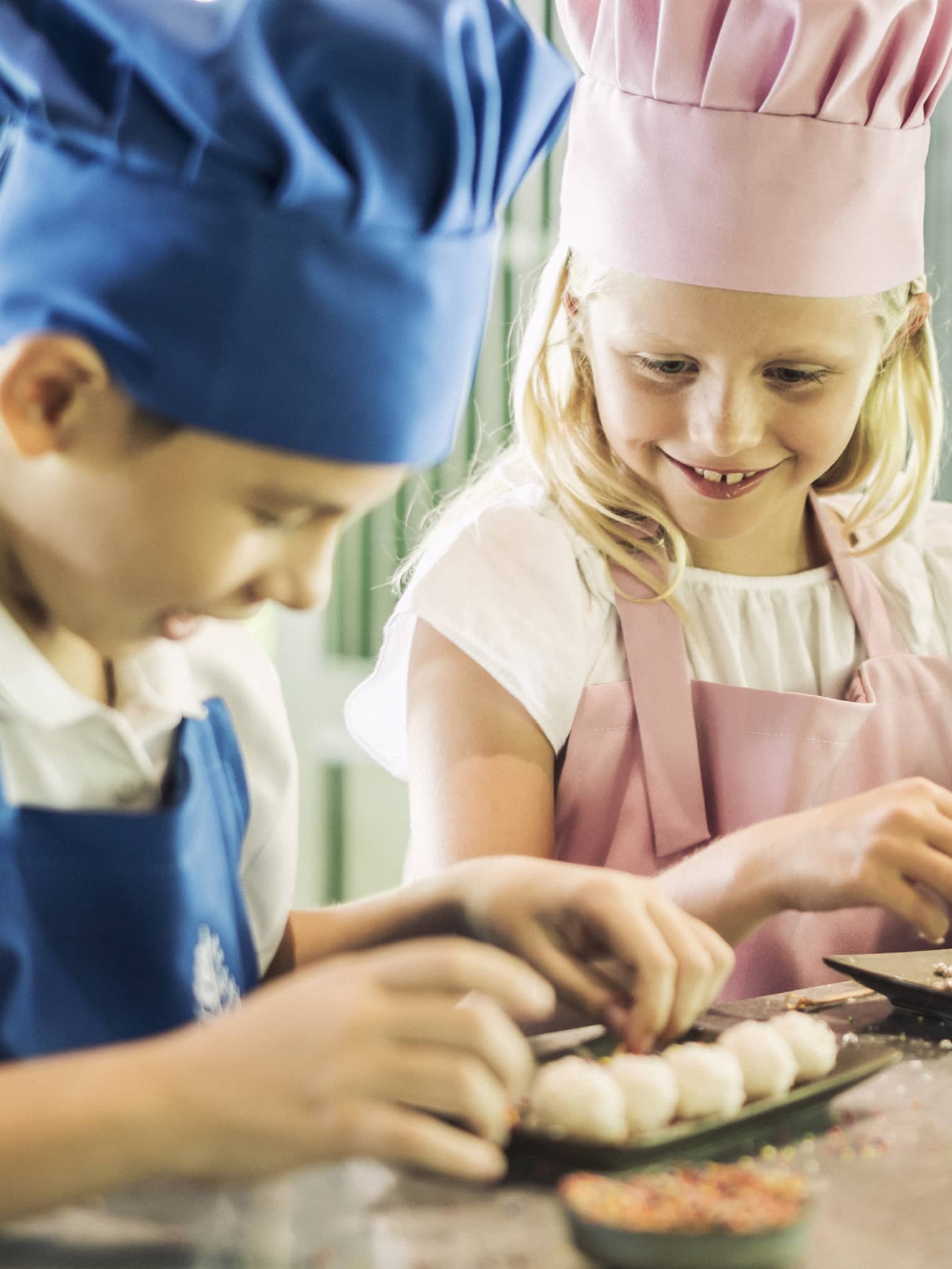 Three children in chef hats, aprons roll pastries at counter