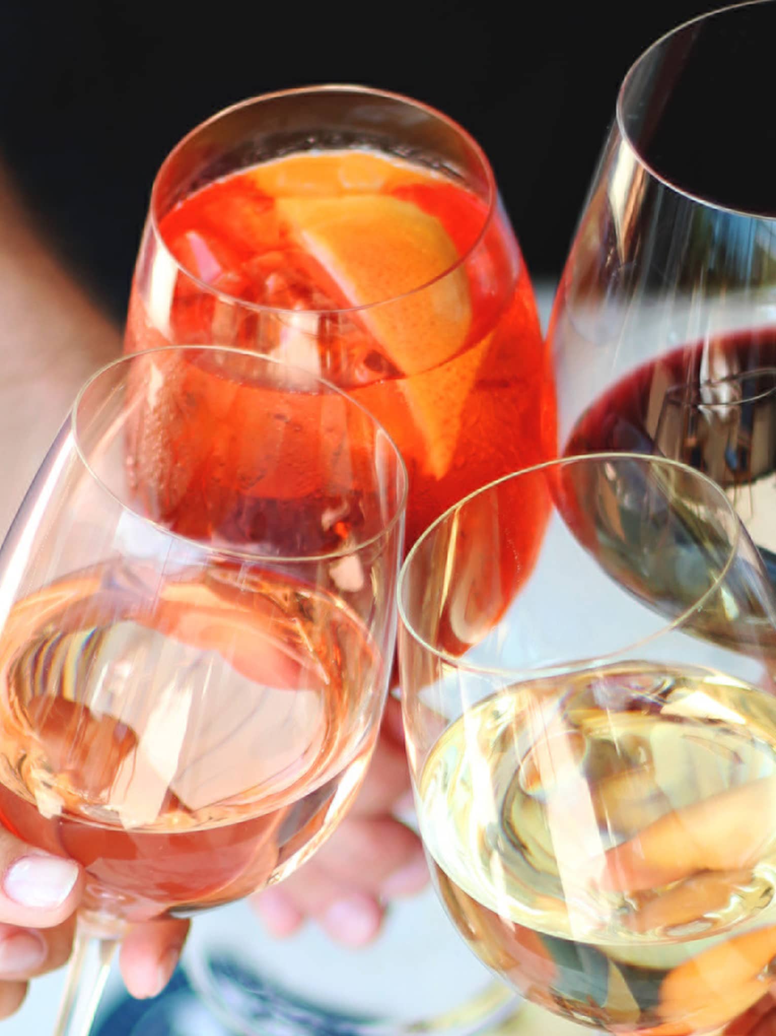Four hands toasting with different kinds of wine above charcuterie platter