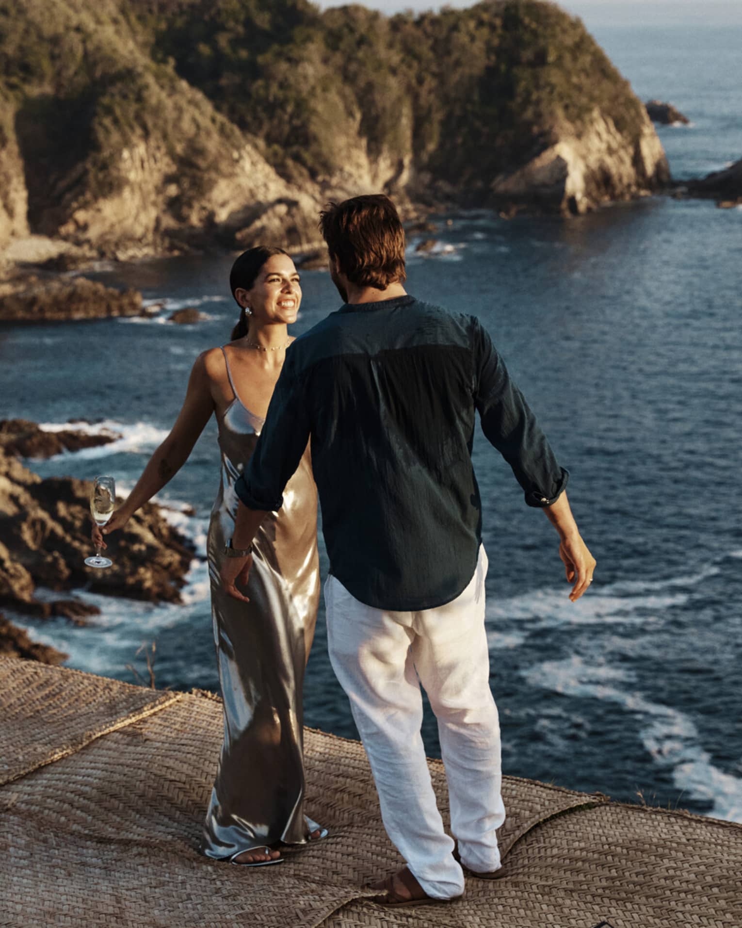 A couple standing near a vast, shimmering ocean against a backdrop of majestic cliffs, embraced by the beauty of nature