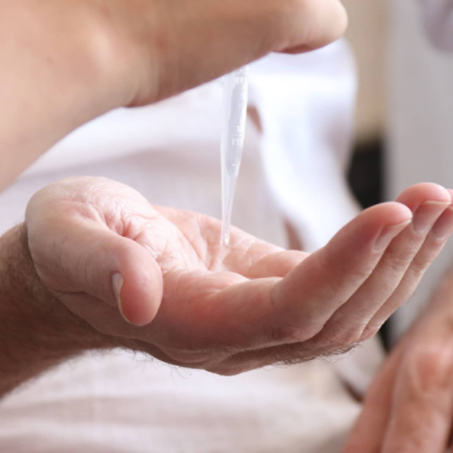 A person holding out their hand while another person uses a syringe to drop an aromatherapy blend in their hand