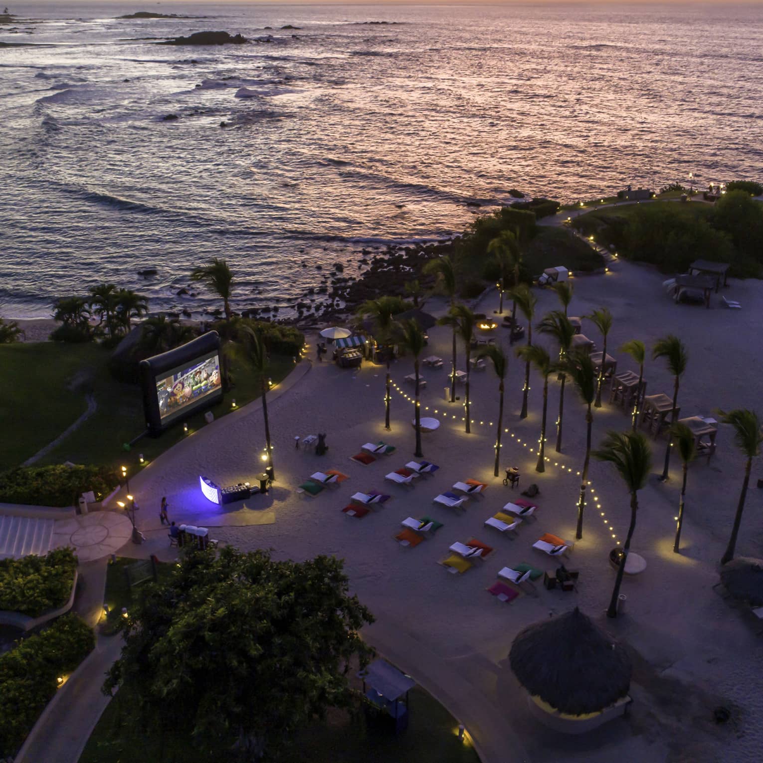 A bird's eye view of cars watching. a screen on a beach.