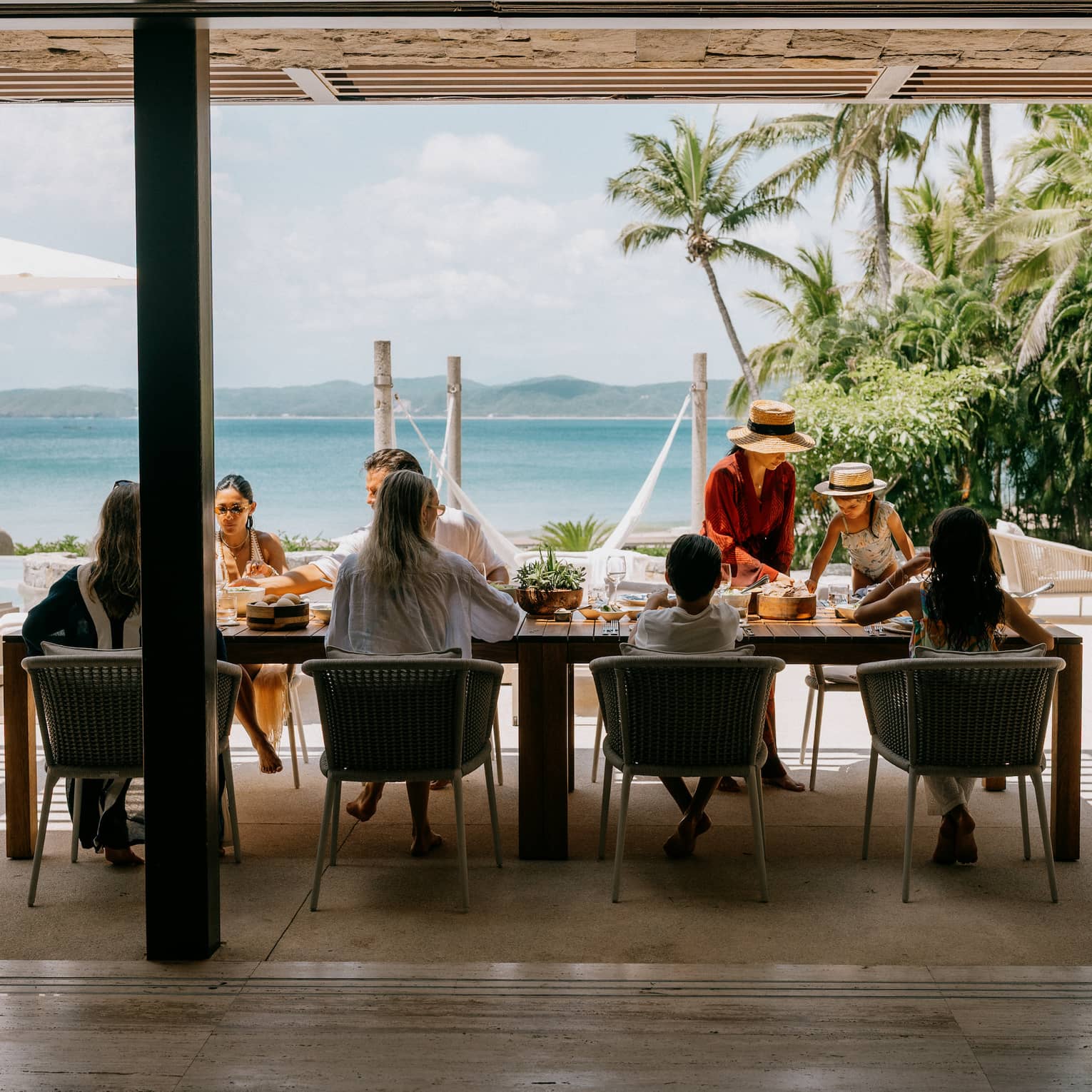 A group of people enjoy a meal in an outdoor dining setting looking out over the beach and ocean.
