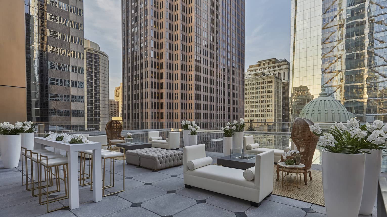 The outdoor Ballroom terrace is decorated with a silver table lined with white flowers, white couches, a rattan chair and jute rug and and overlooks Philadelphia