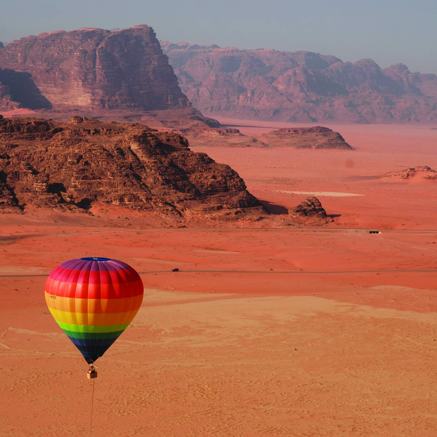 Rainbow hot air balloon flying over red sand in Jordan desert