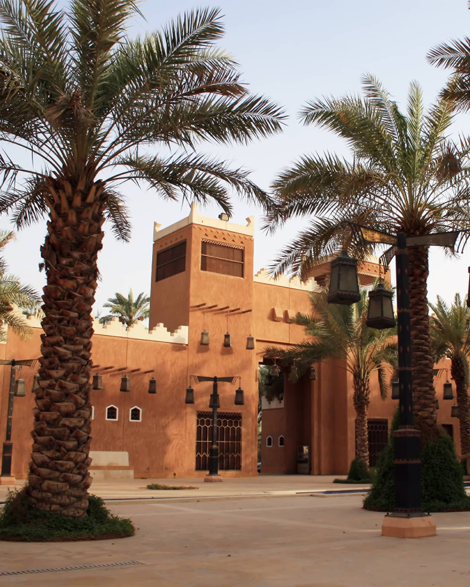 Sunny exterior of sandstone building and large palm trees with lanterns hanging from branches