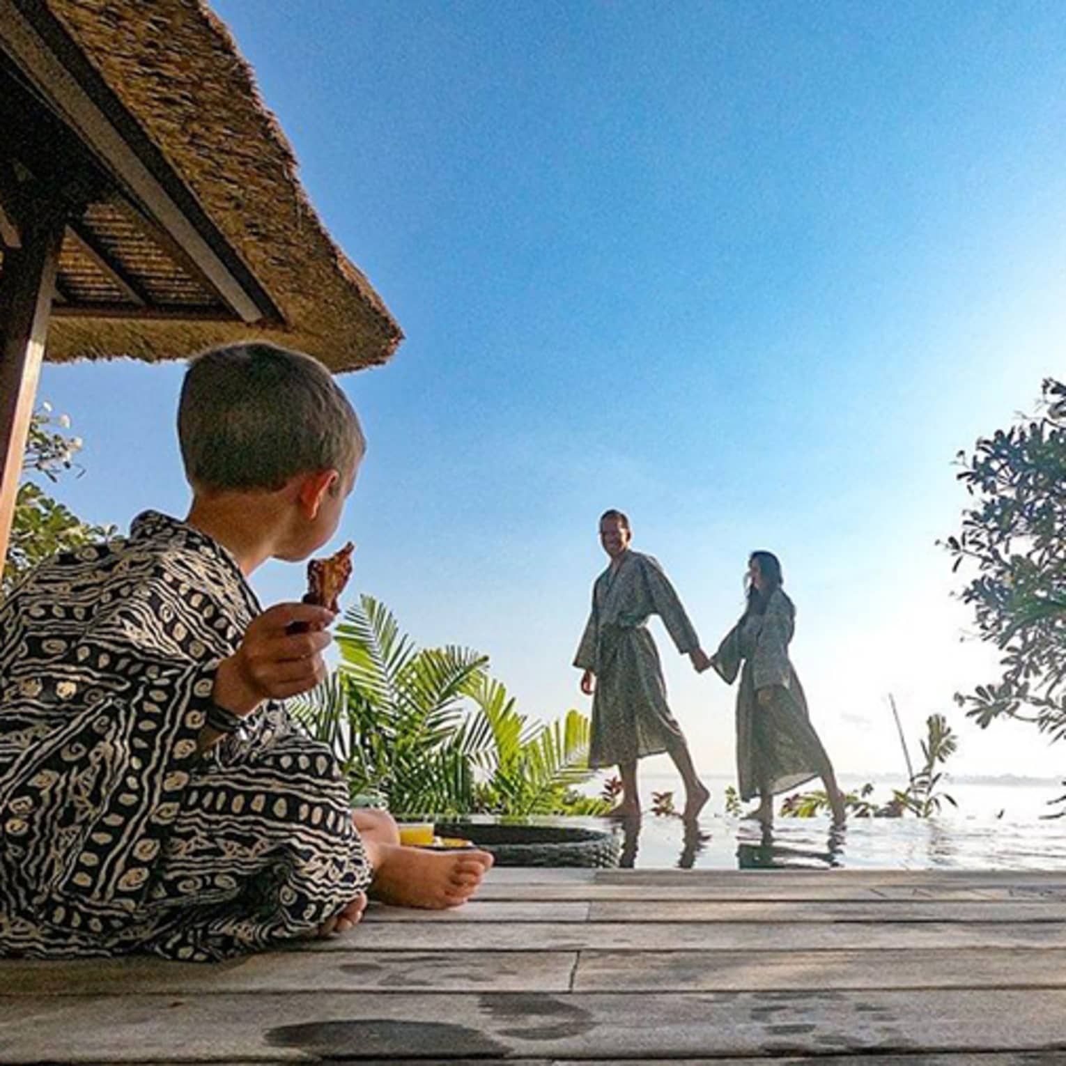 Family wearing robes, young child sits cross legged on patio as parents hold hands in background