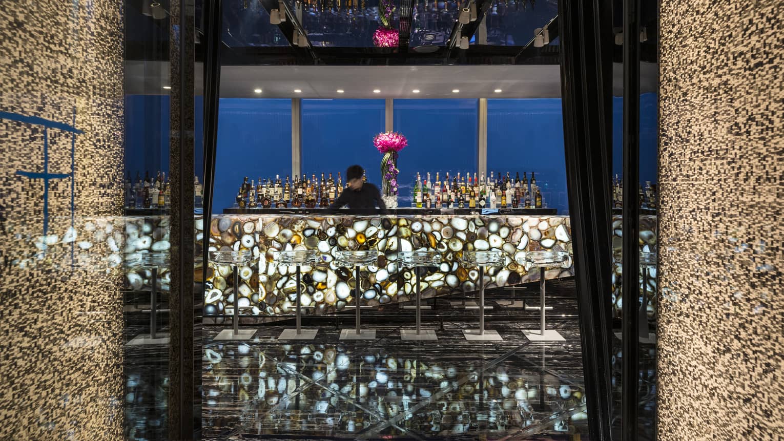 Tian Bar bartender behind bar with illuminated multi colored agate stone, modern clear stools