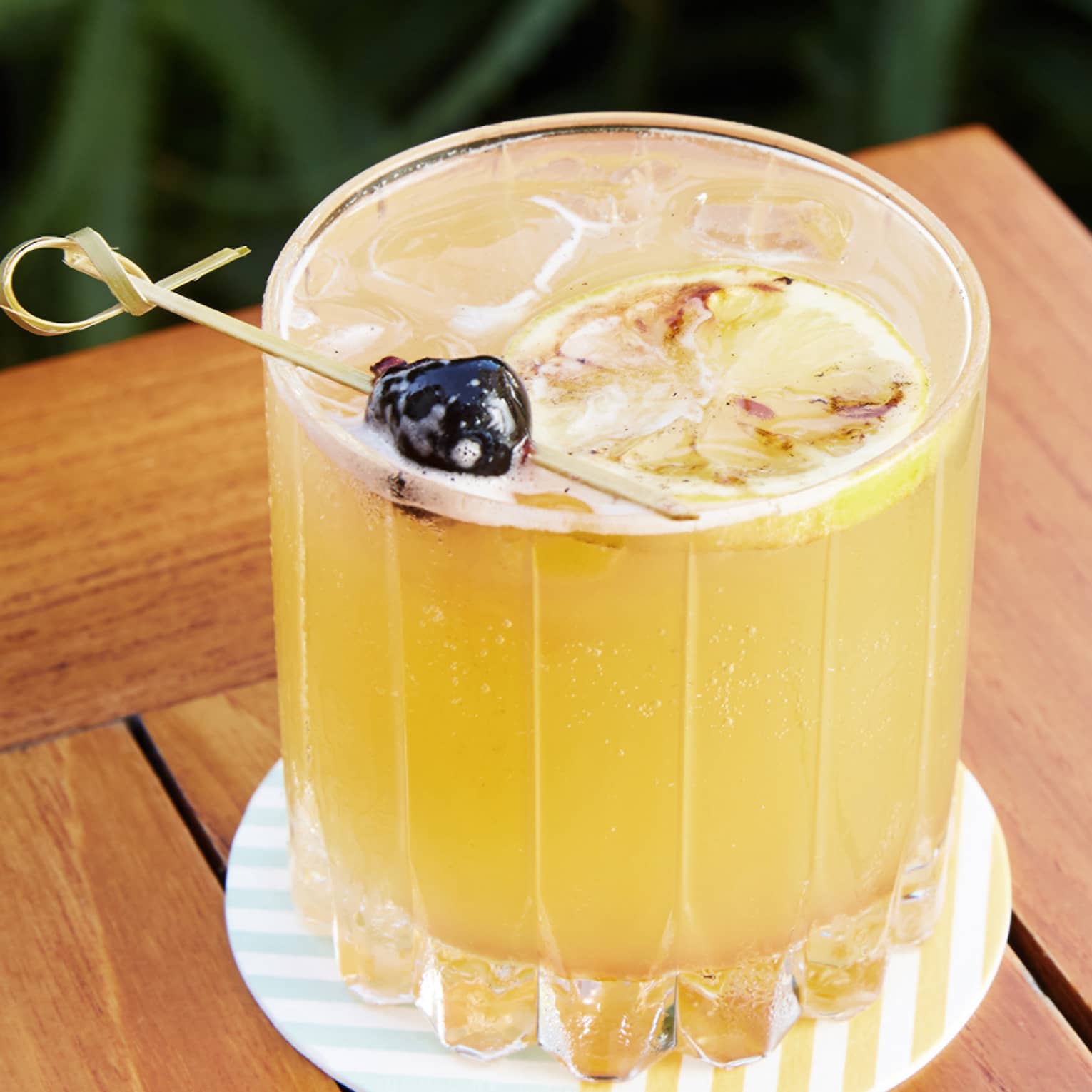 Yellow drink in a glass on a coaster on an outdoor table.