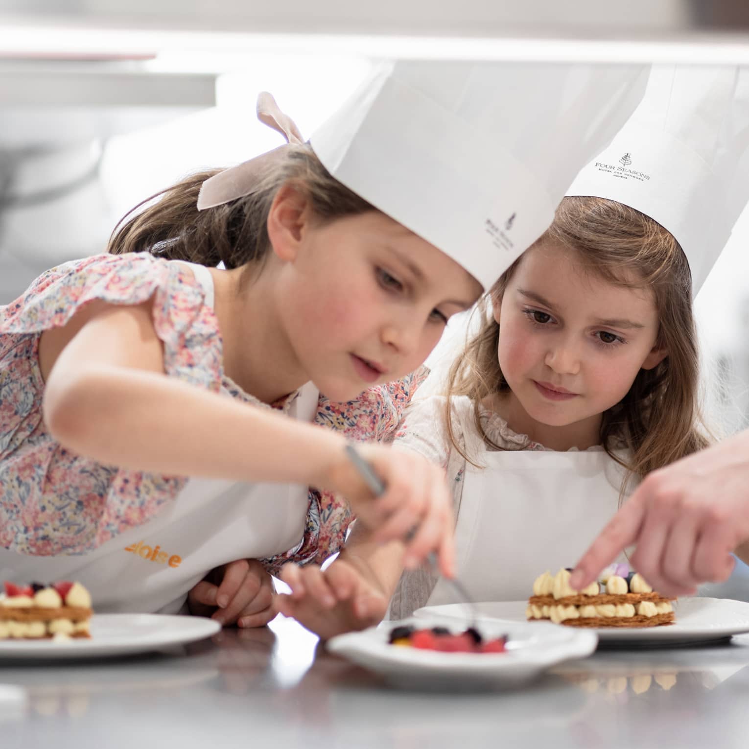 Two children in chef hats carefully decorating plates of desserts during a pastry-making class