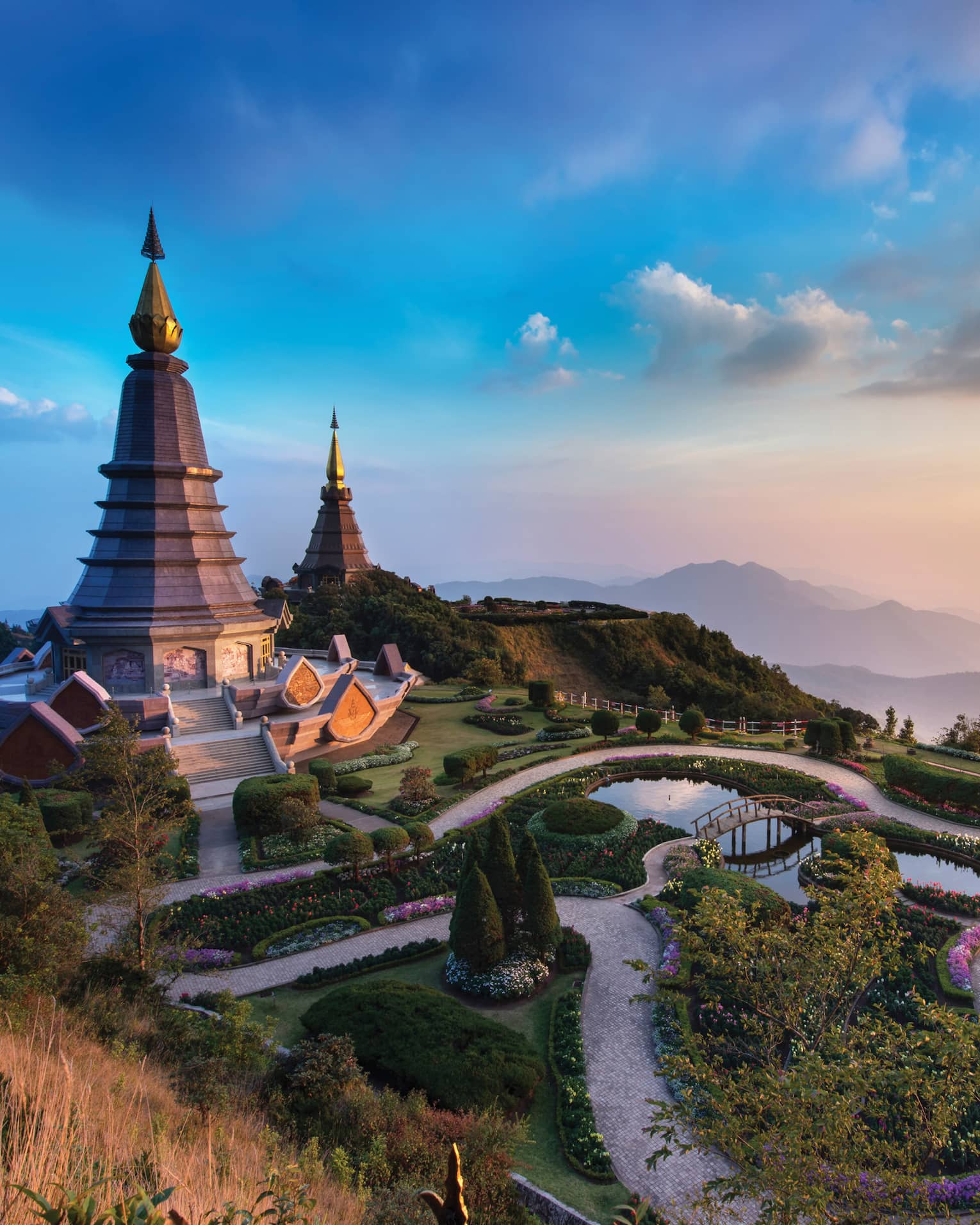 Majestic twin pagodas surrounded by lush gardens and winding paths, set against a backdrop of misty mountains at sunset.