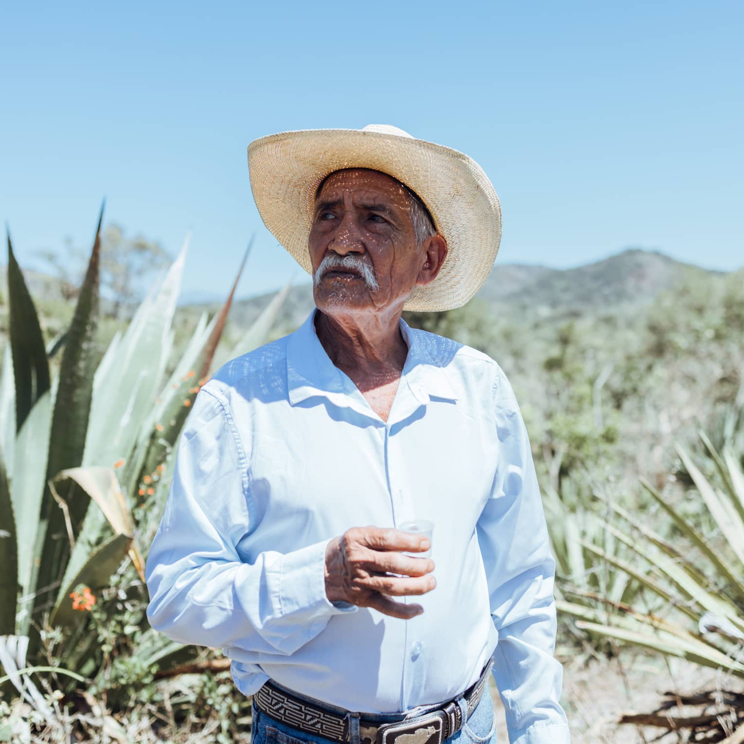 Person wearing a hat and a blue button down shirt standing outside.