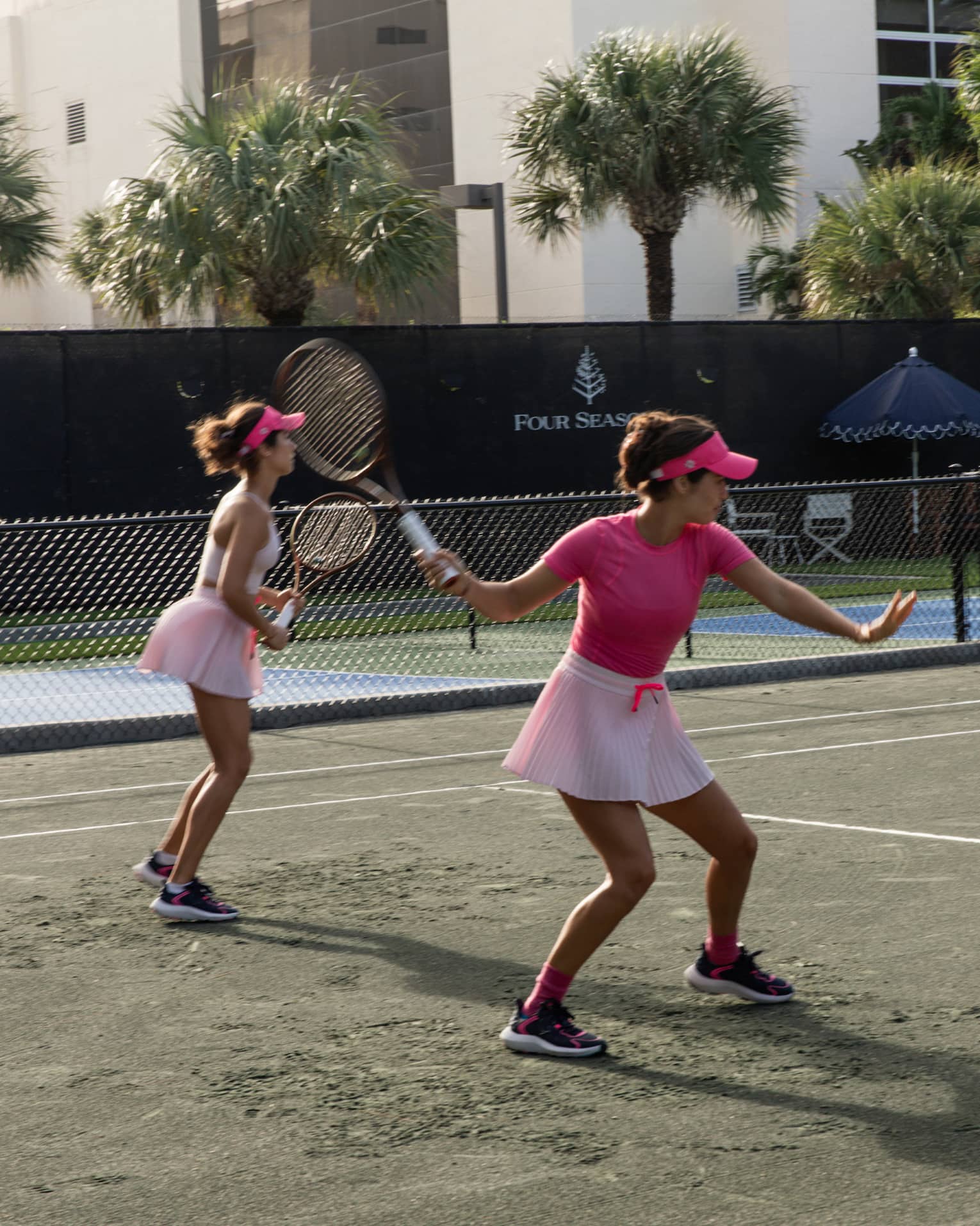 Two tennis players both wearing pink volley on a clay court