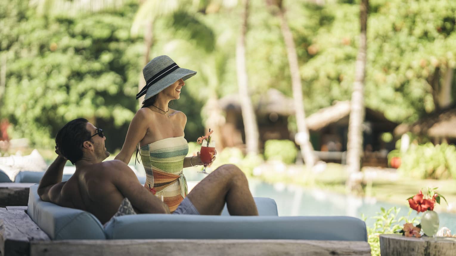 A couple drinking cocktails while lounging on an outdoor chair by a pool