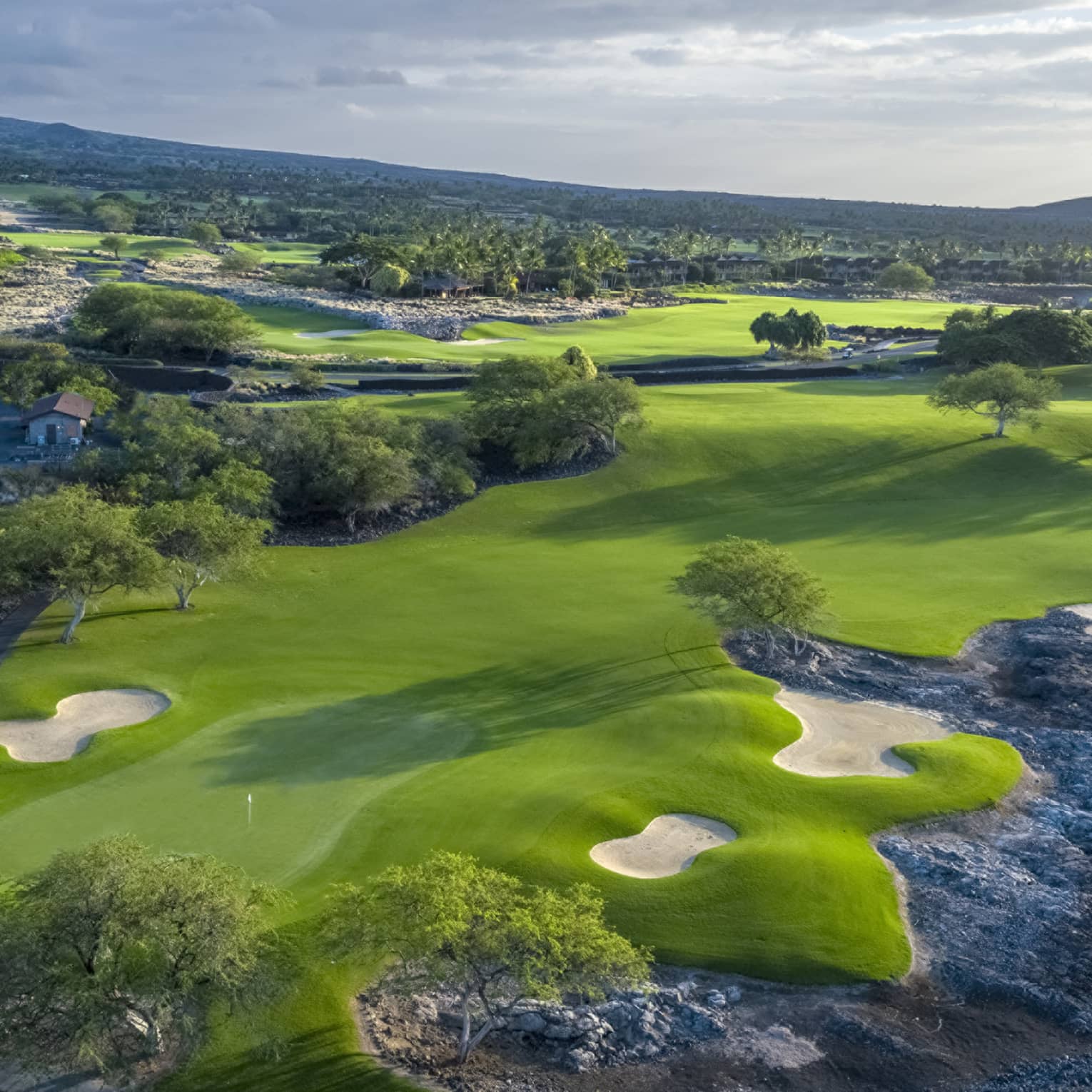 An overhead view of a lush green golf course under a cloudy sky.