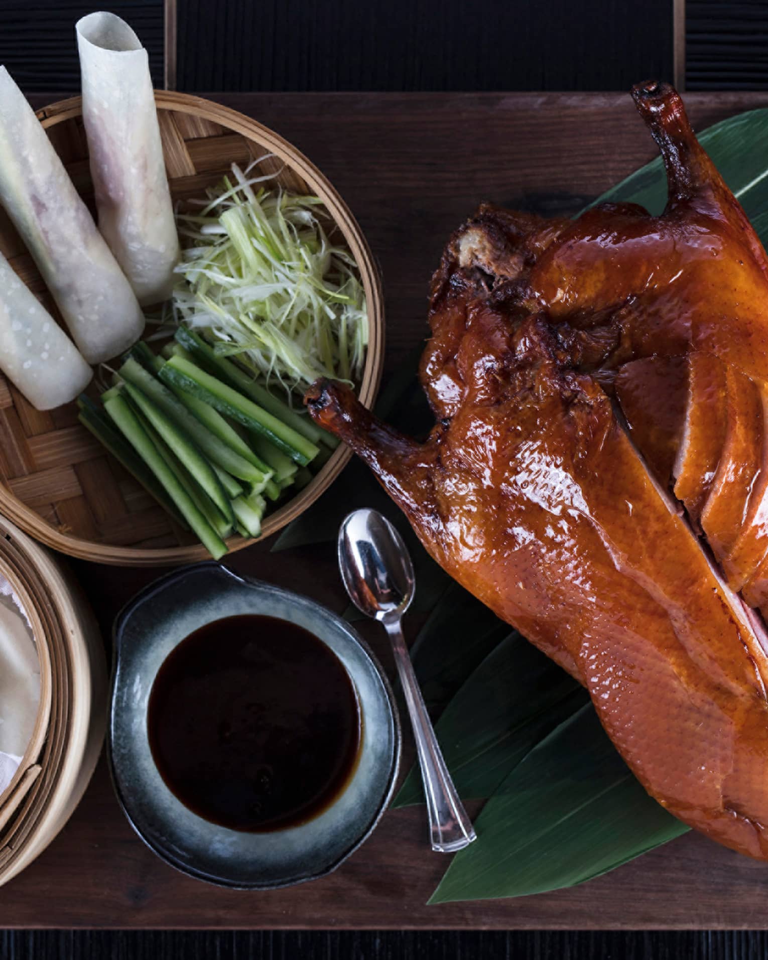 Aerial view of Peking Duck sliced on side, bamboo basket with spring rolls, onions