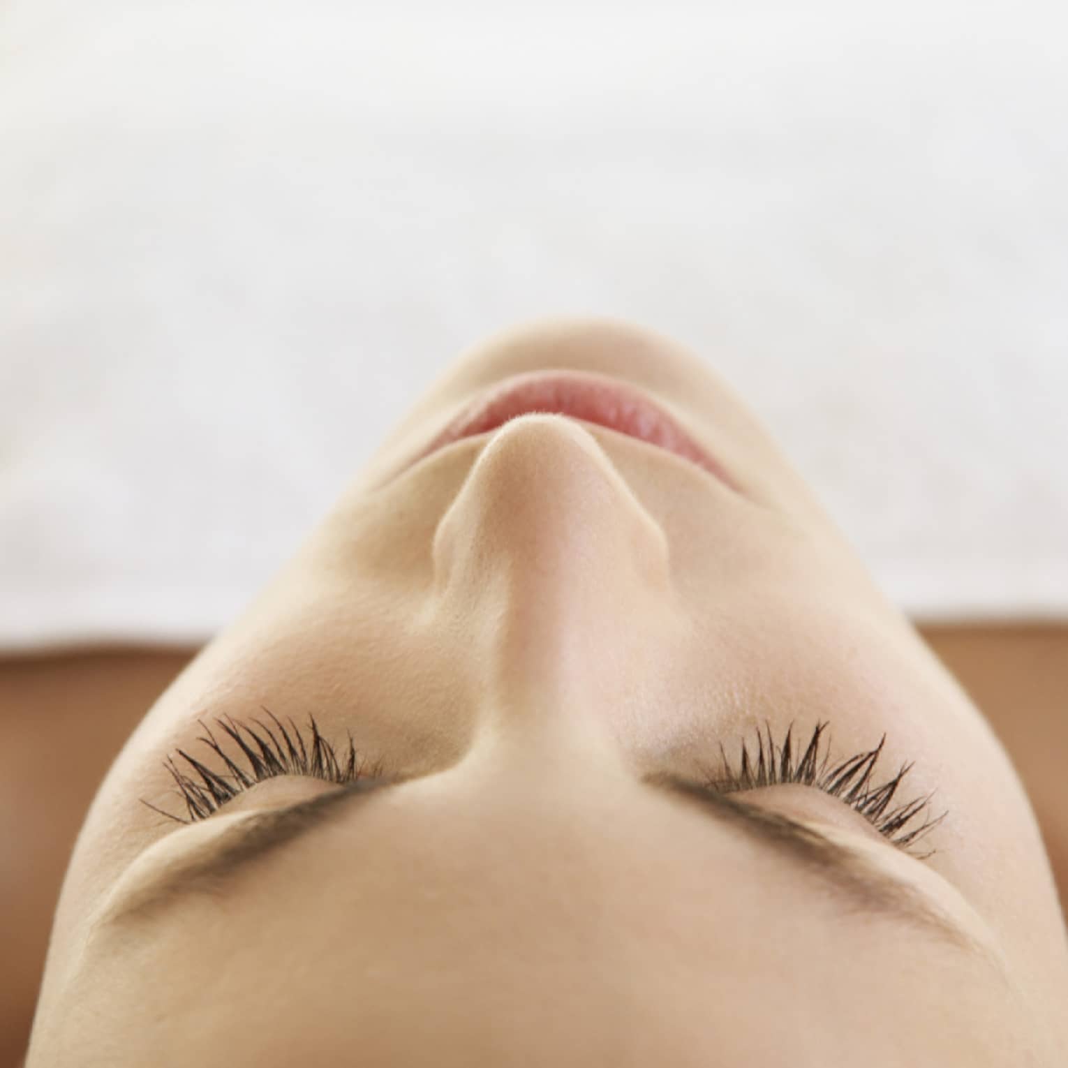 Woman lying down with eyes closed, bare shoulders, covered with white sheet
