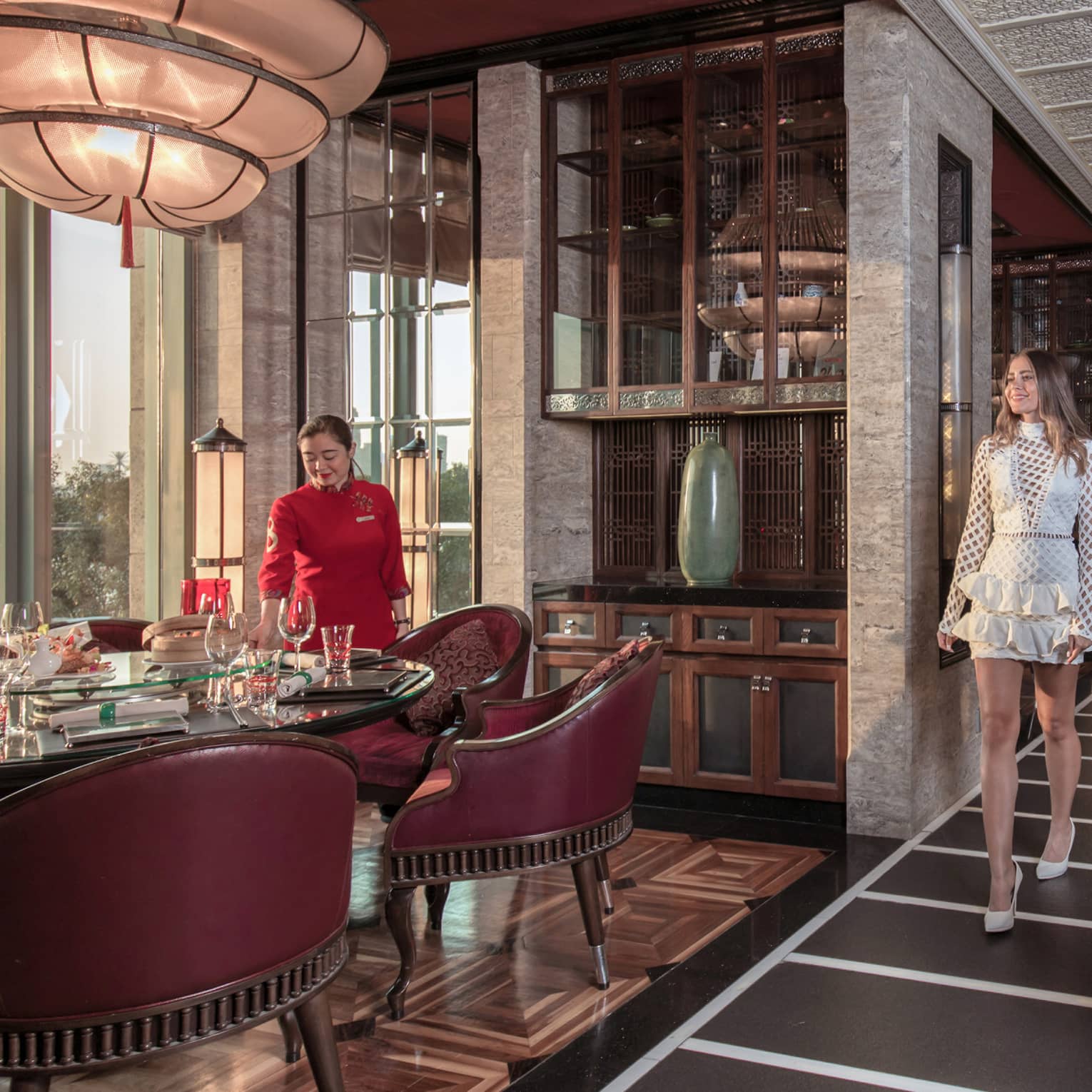 A guest is shown to her table, surrounded by burgundy chairs, in a luxurious restaurant with opulent decorations.