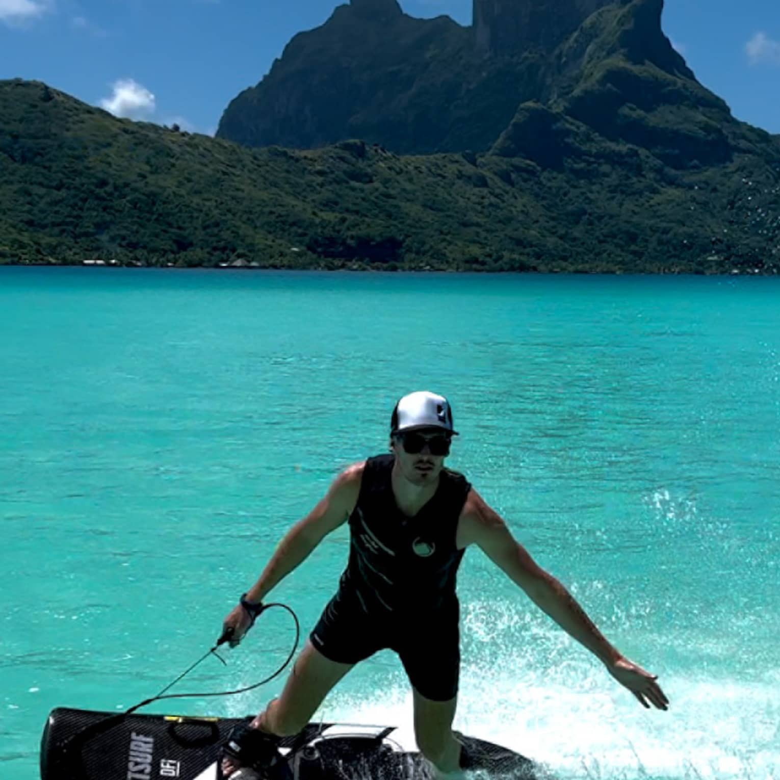 Person on JETSURF board rides on turquoise water, mountain visible in background
