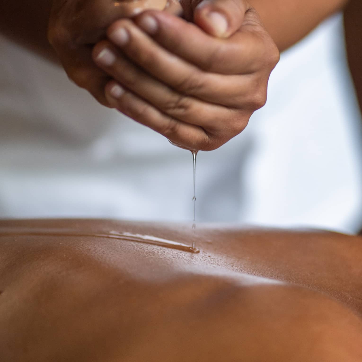 Delicate hands apply oil to a guest's back during a spa treatment