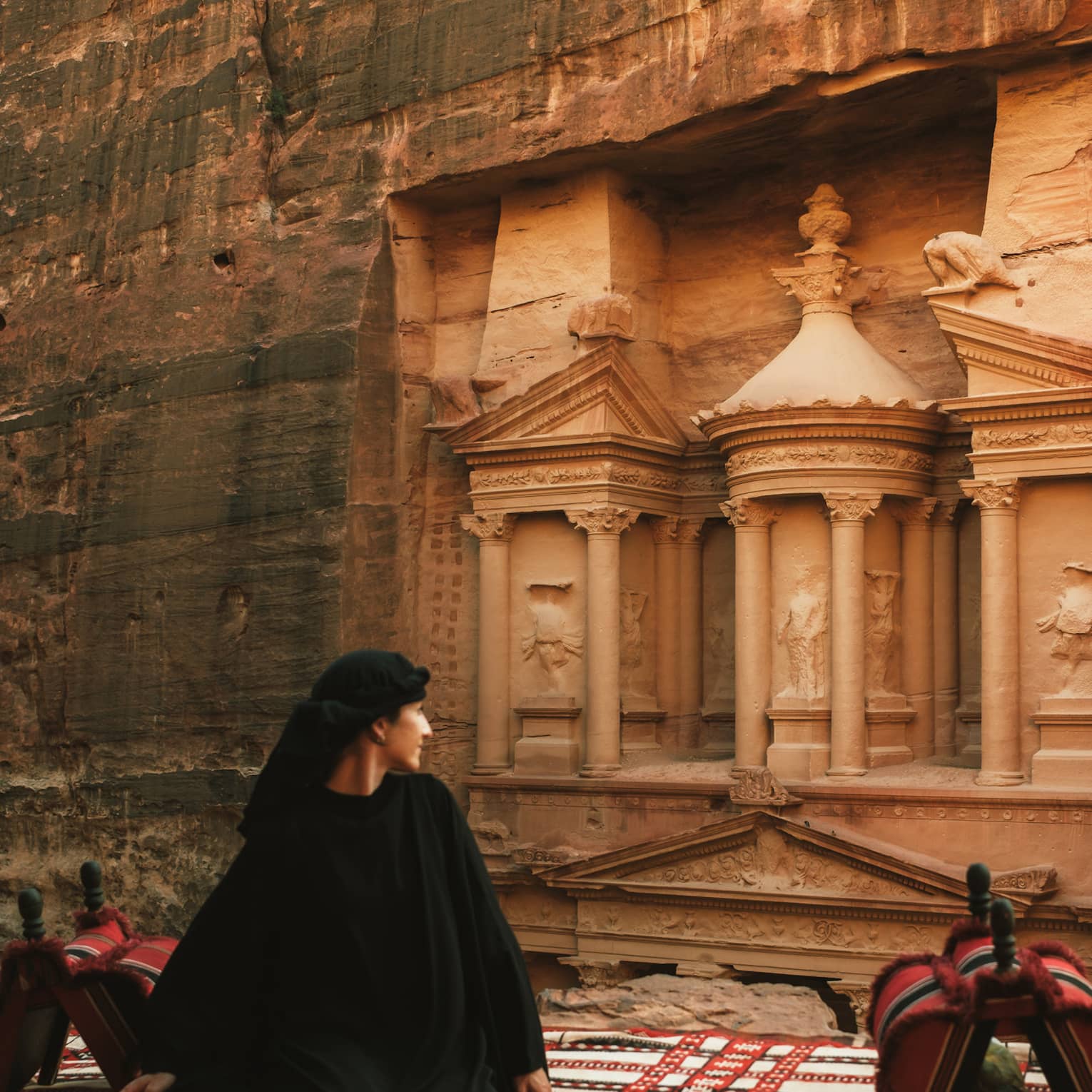 A person stands looking at buildings carved into a red rock cliffside.