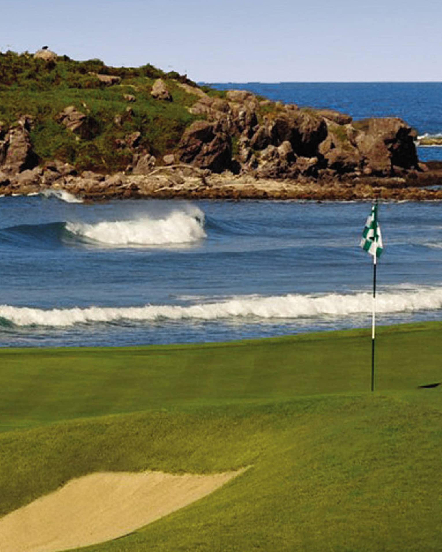 Bahia Golf Course flag on green beside rolling ocean tide, large rock