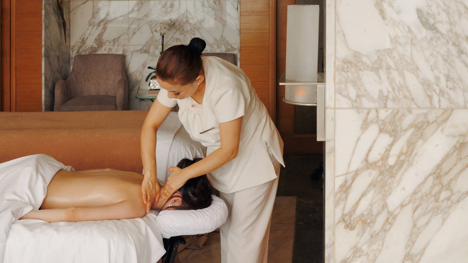 A female spa therapist performing a massage on a woman, face down on spa treatment table, in a chic luxury spa with marble walls