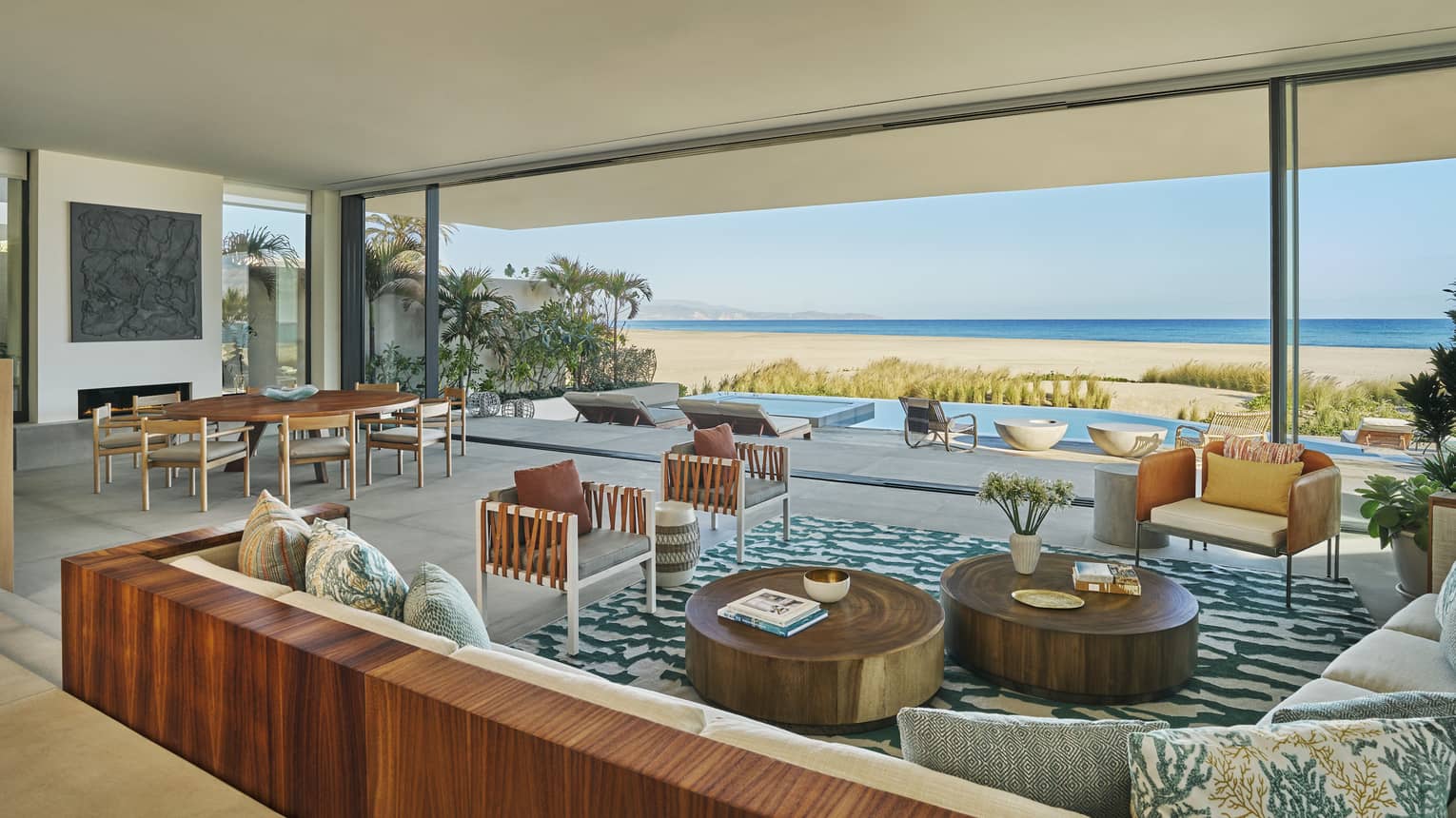 Expansive living and dining room of a private luxury villa with modern Baja design, at Four Seasons Resort and Residences Los Cabos. A huge wall opens to a private pool deck, with sea and beach views.