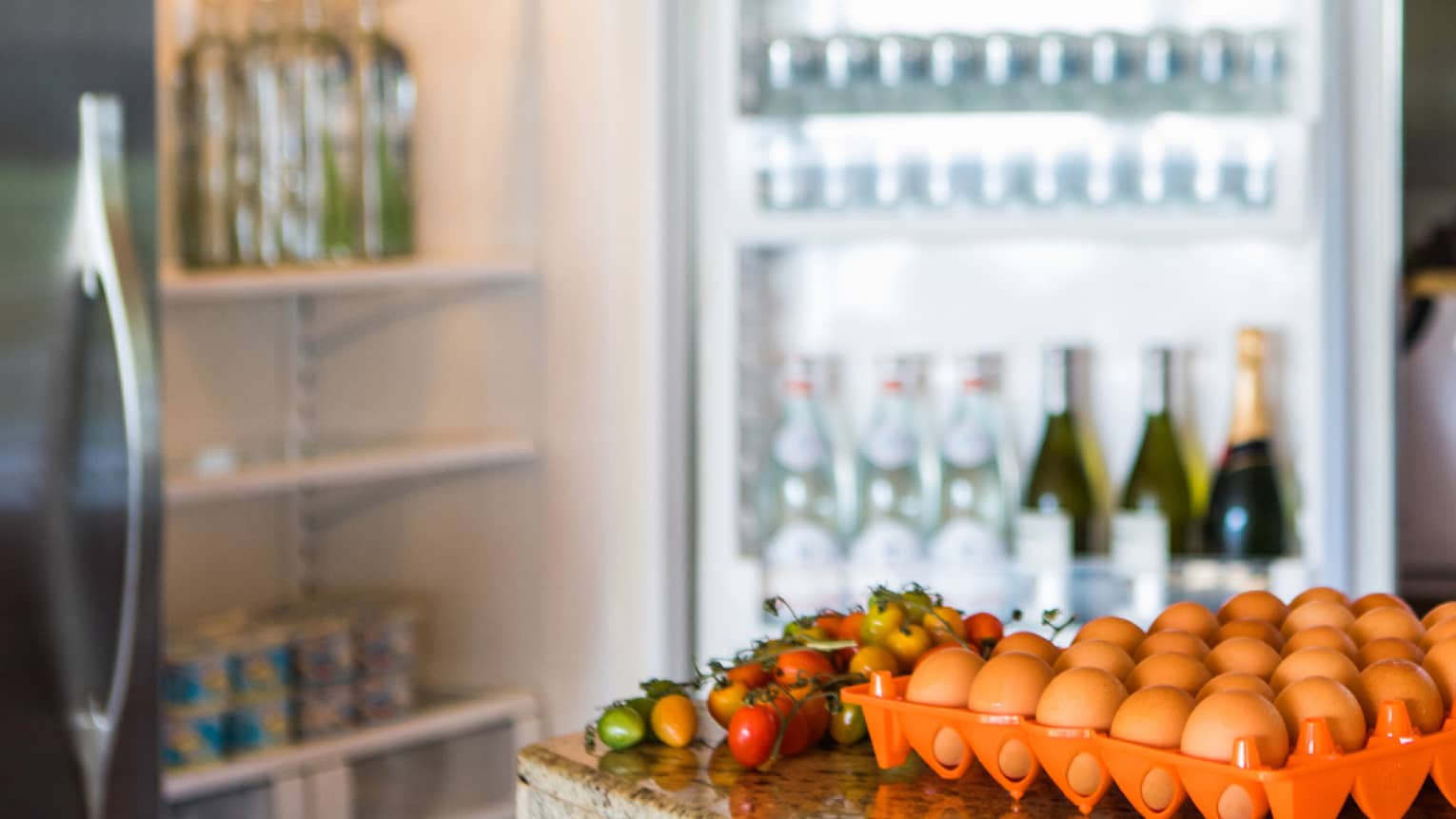 Smiling man holds green bottle in front of open fridge, fresh eggs on counter
