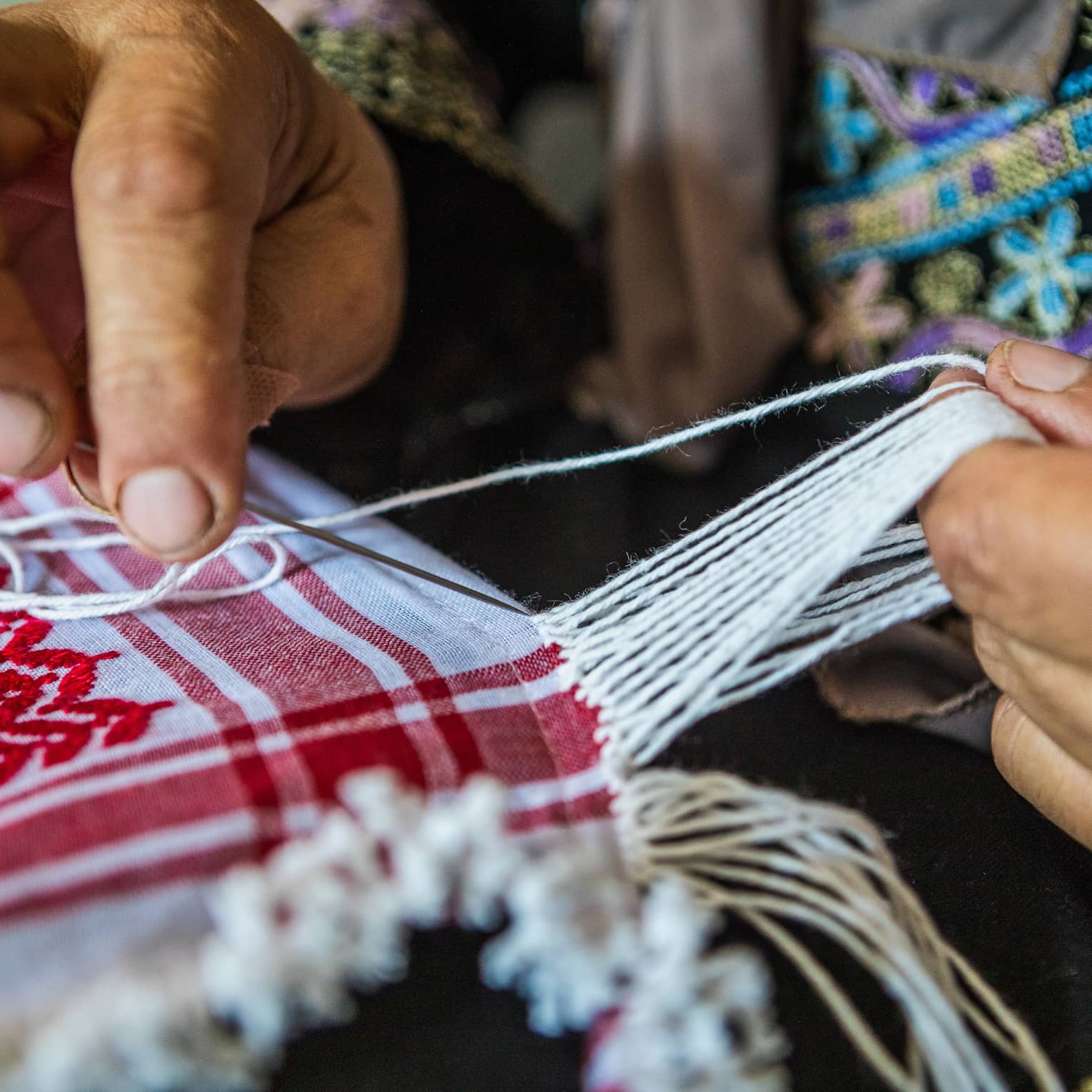 A person weaving strands of fabric together to create a quilt.