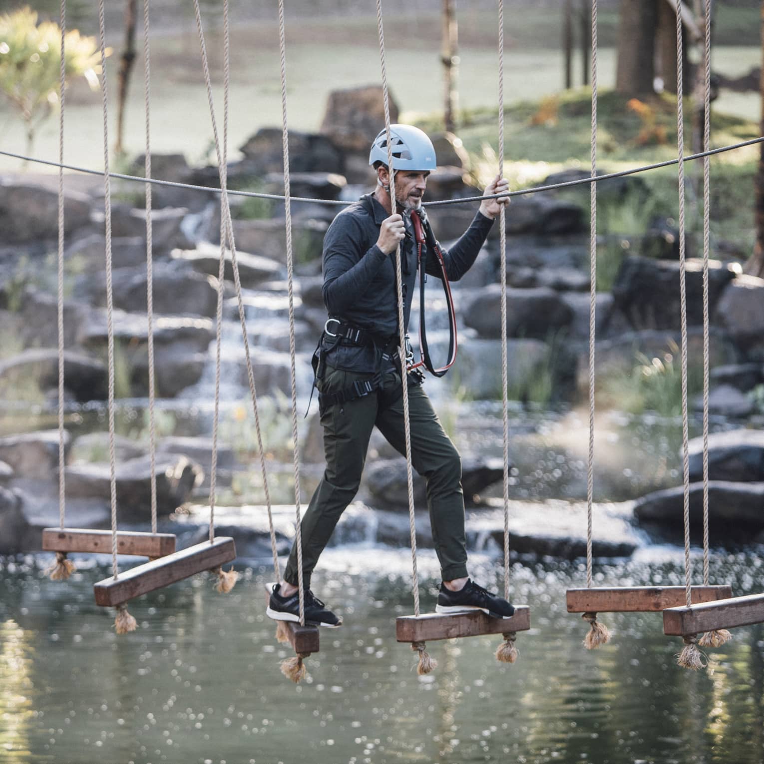 A man walks across hanging wooden blocks at ropes course