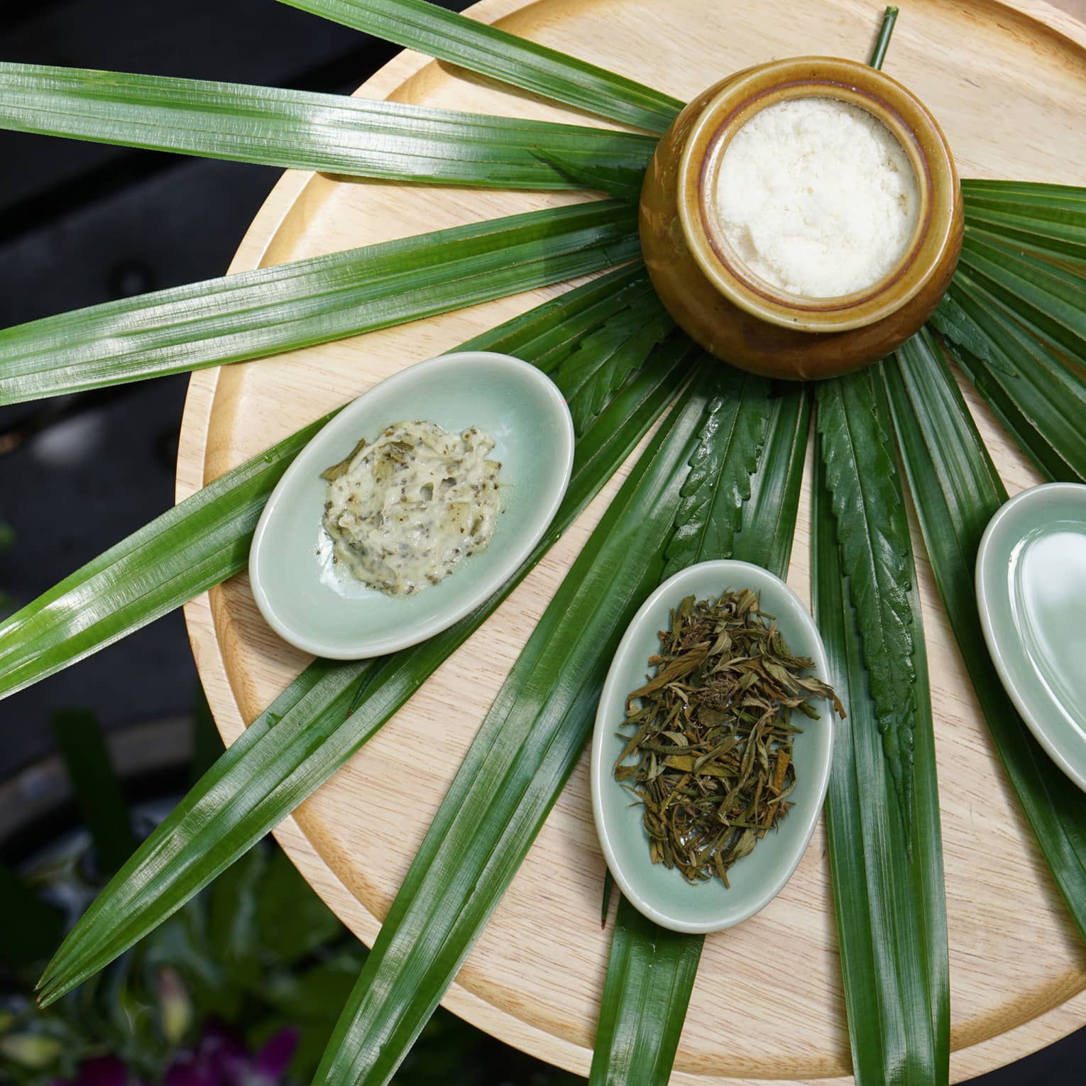 Pandan leaves laid out like a fan on a wooden table with a jar and small bowls of herbs and scrubs placed on top.