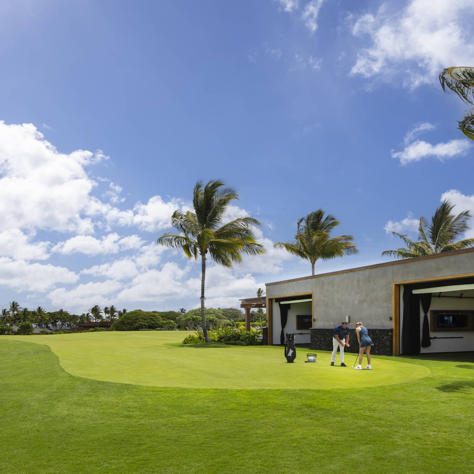 A woman receives an individual golf lesson on a golf course outside a building with palm trees.