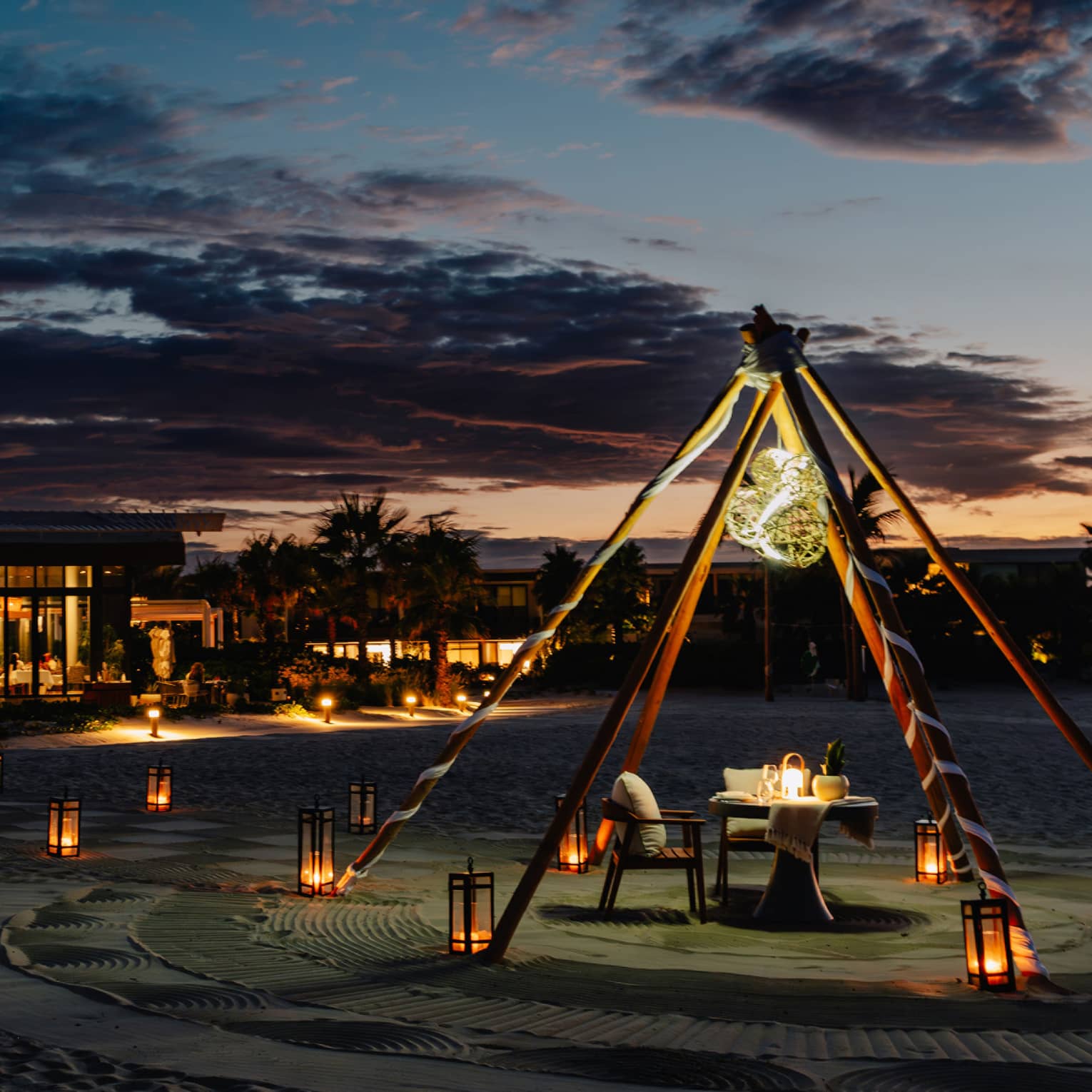 Outdoor tent with a chair and dining table, surrounded by lanterns on the ground in the evening.