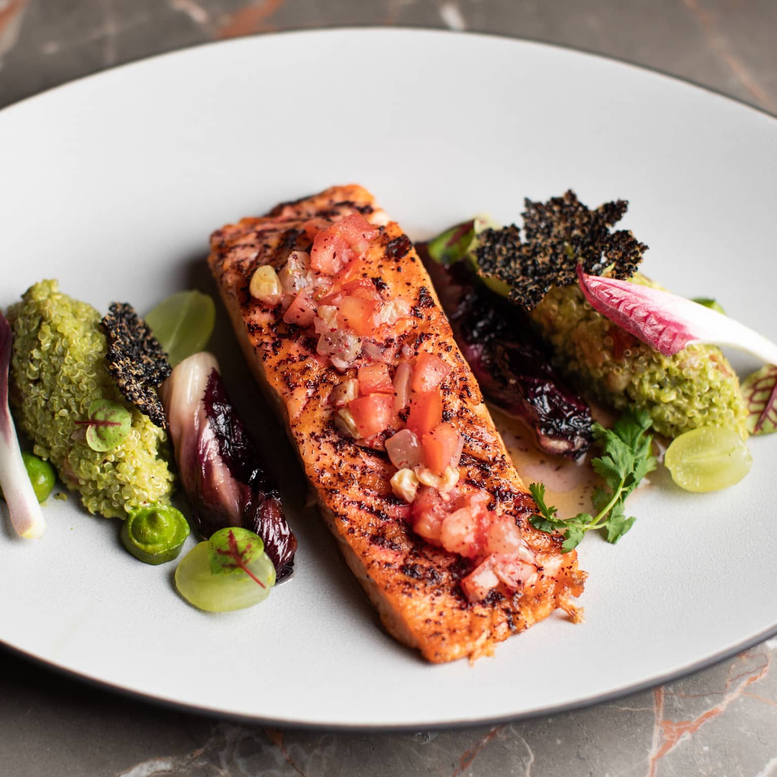 Fish fillet topped with salsa and served with green vegetables on a white oblong dish