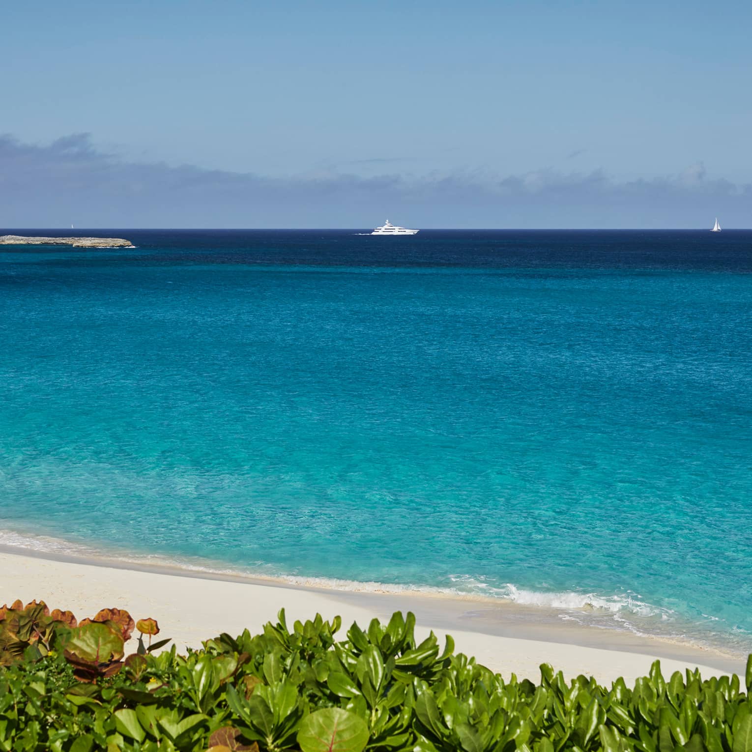 Turquoise ocean by white sand beach, yacht on horizon against blue sky