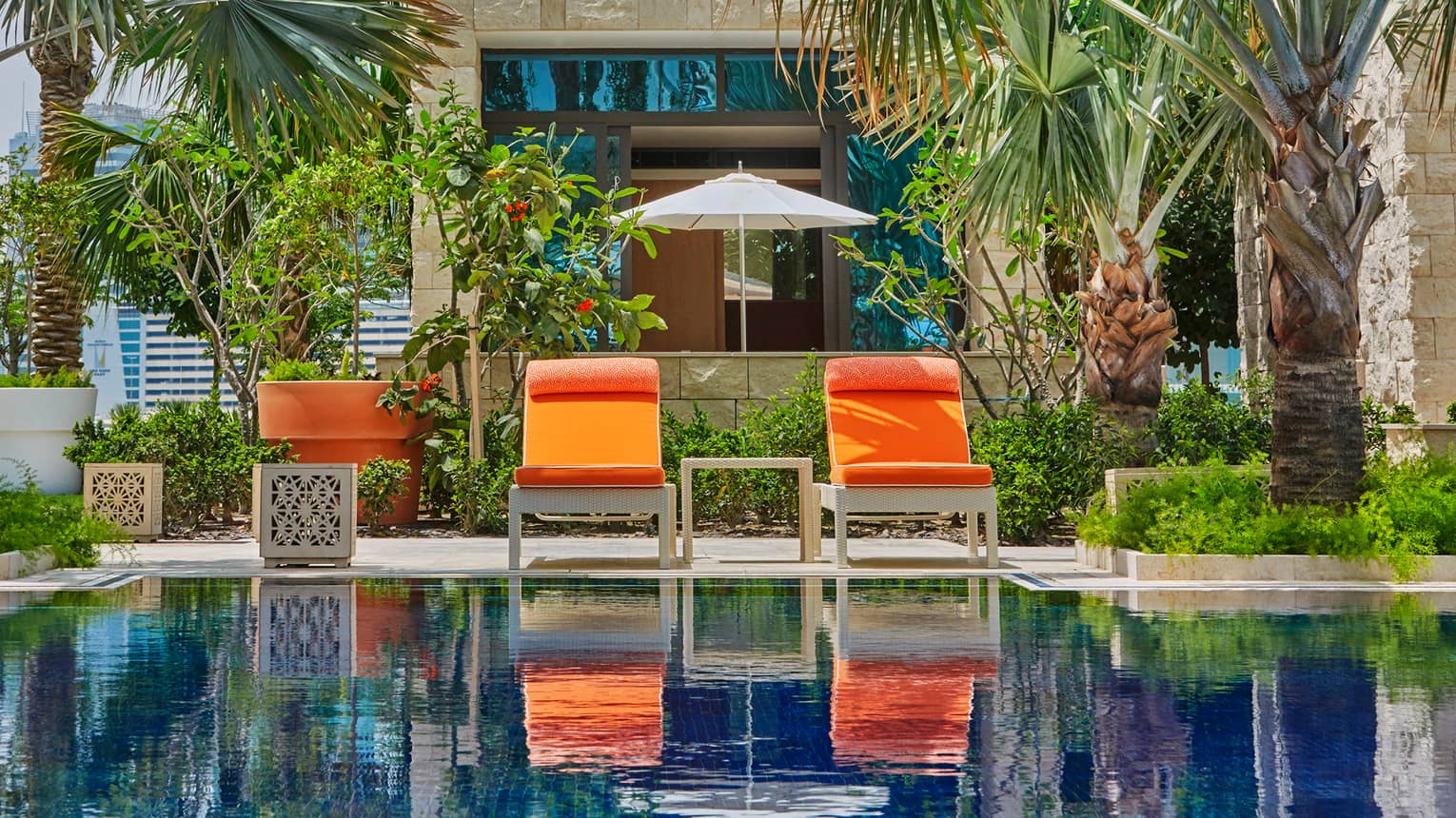 Two orange patio chairs in front of palm trees, tropical garden, swimming pool