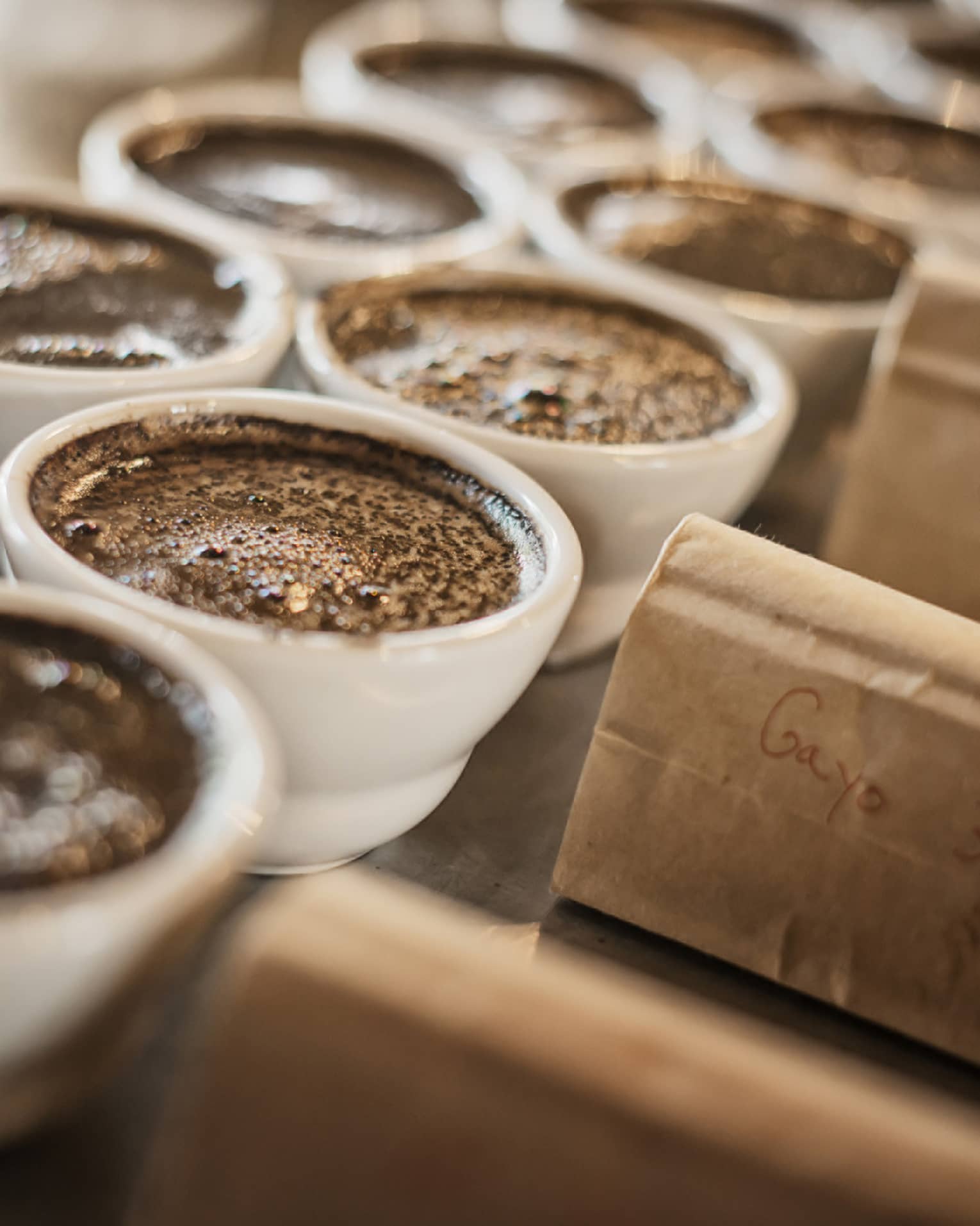 Dark coffee in white porcelain ramekins next to kraft paper bags.
