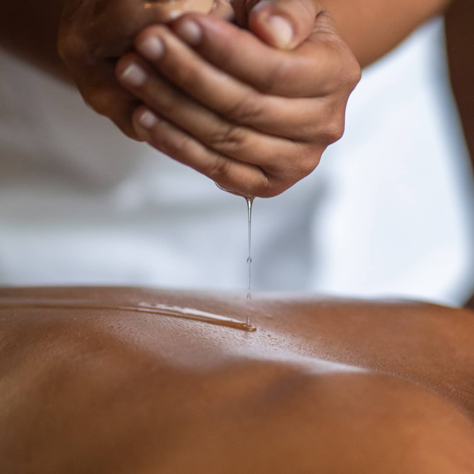 Delicate hands apply oil to a guest's back during a spa treatment