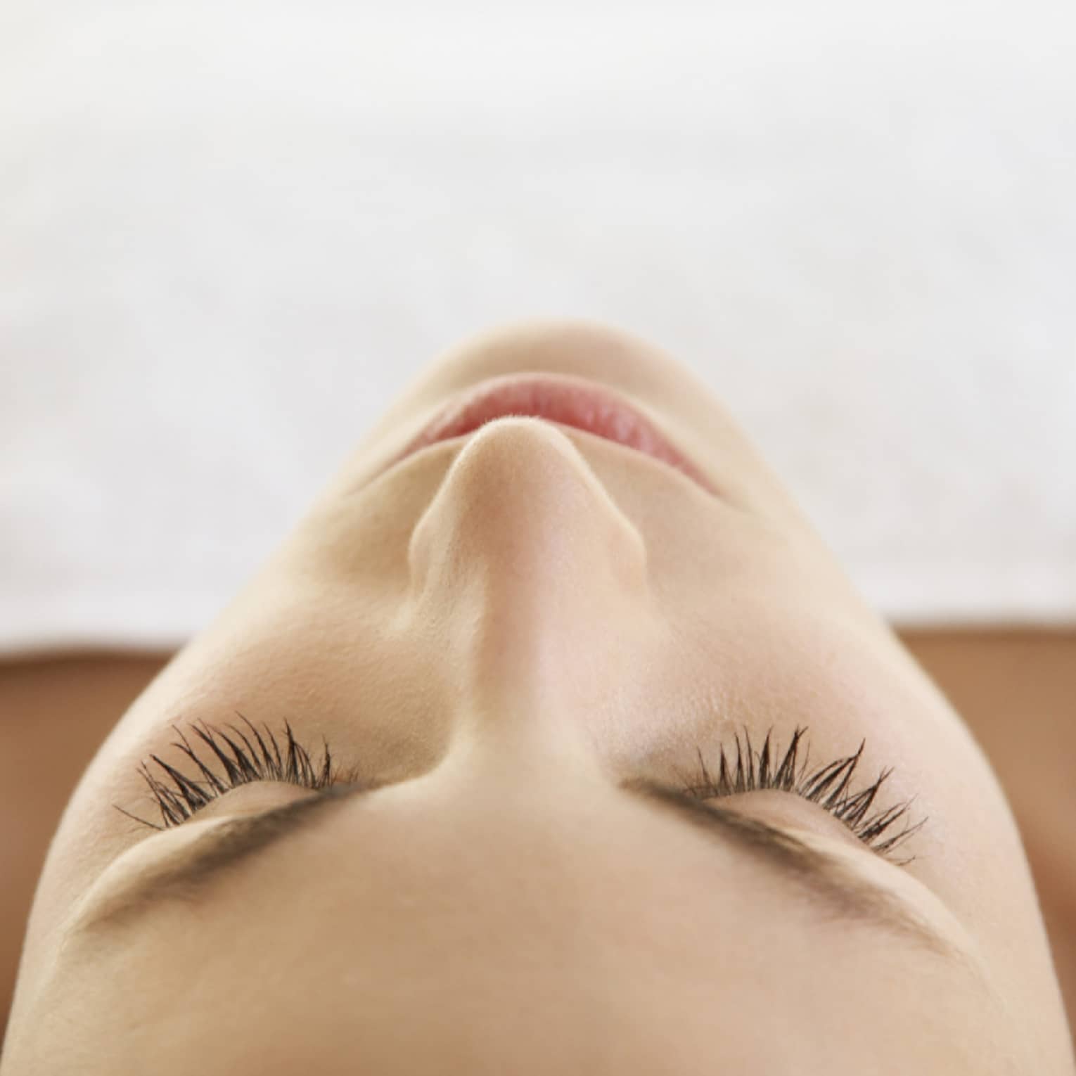 Woman lying down with eyes closed, bare shoulders, covered with white sheet