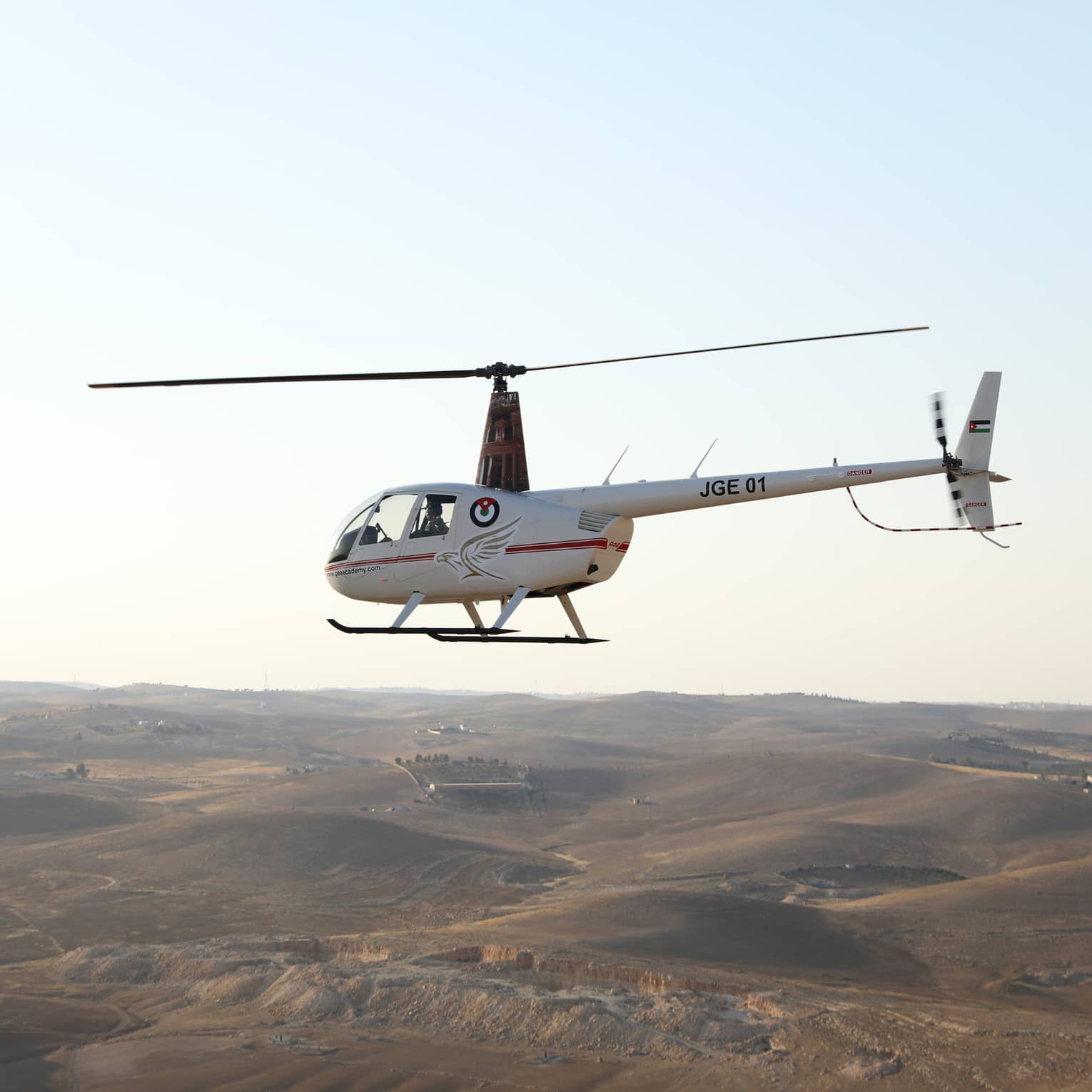 White helicopter flies through the air over rolling hills