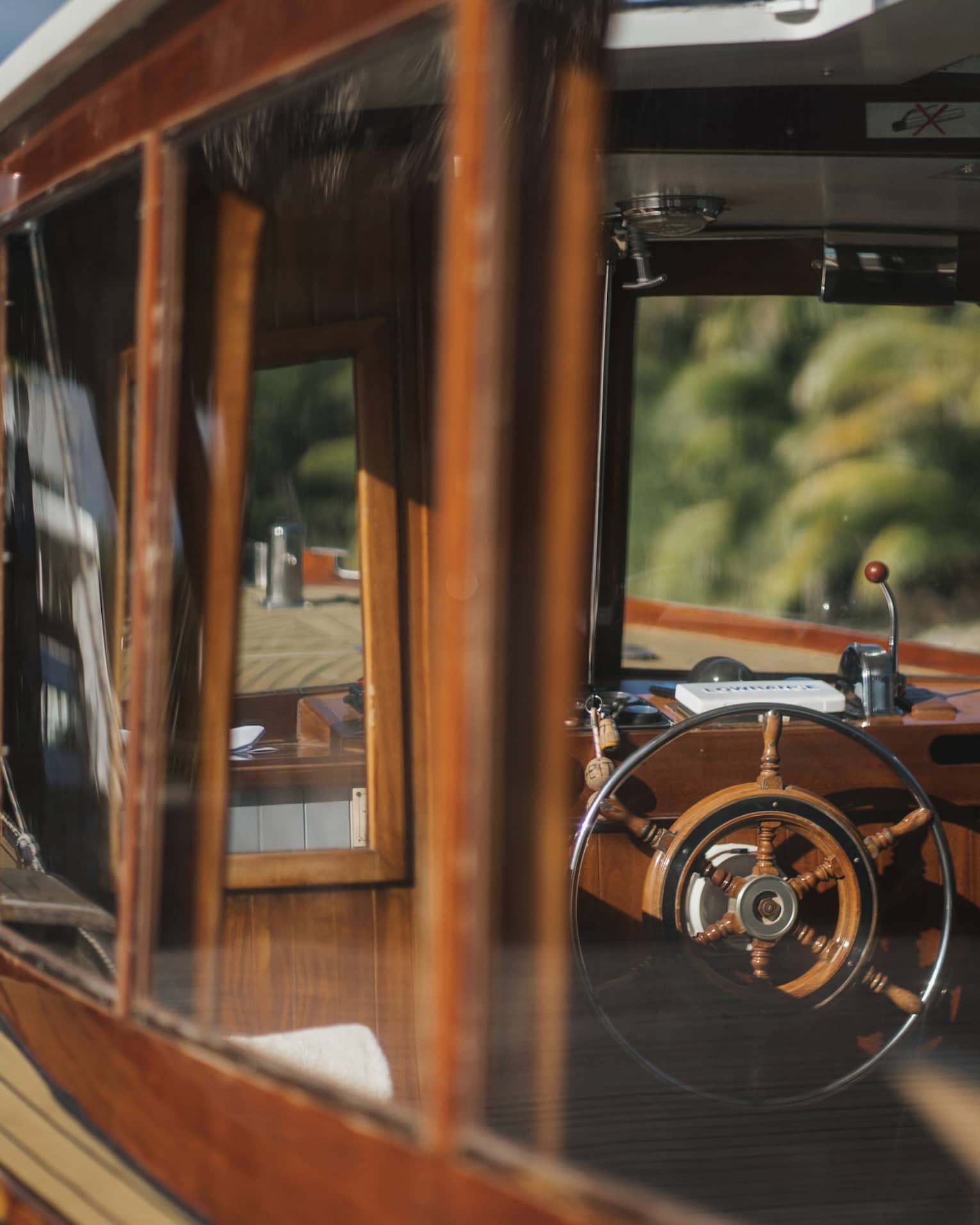 View from outside into a boat's cockpit cabin, both the boat's frame and the wheel partly made of rustic deep-brown wood.