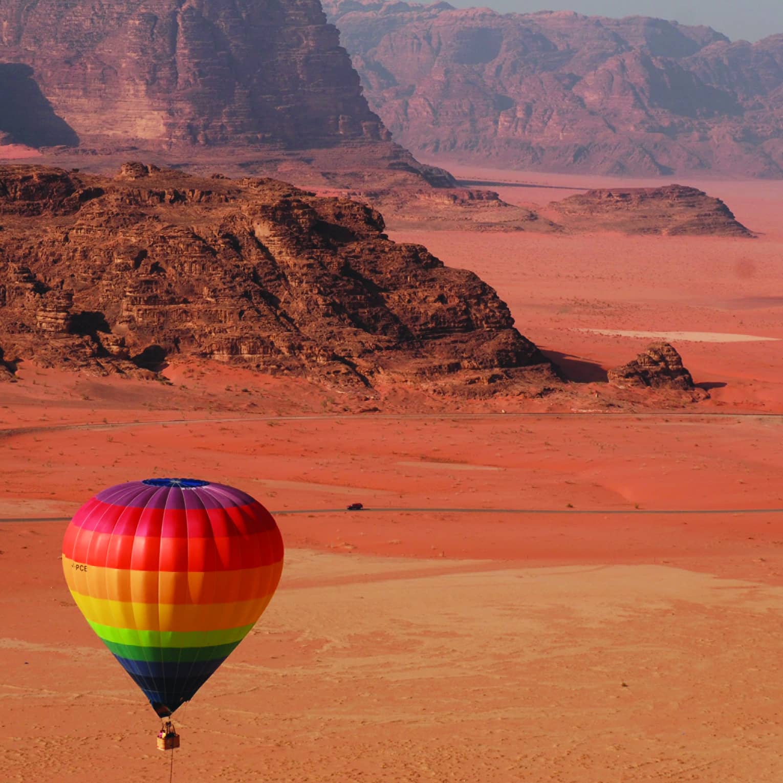 Rainbow hot air balloon flying over red sand in Jordan desert