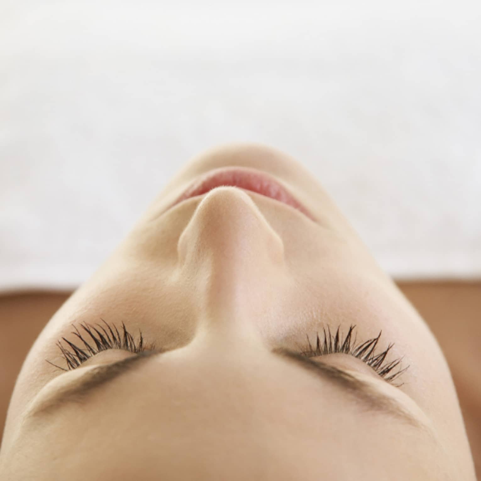 Woman lying down with eyes closed, bare shoulders, covered with white sheet